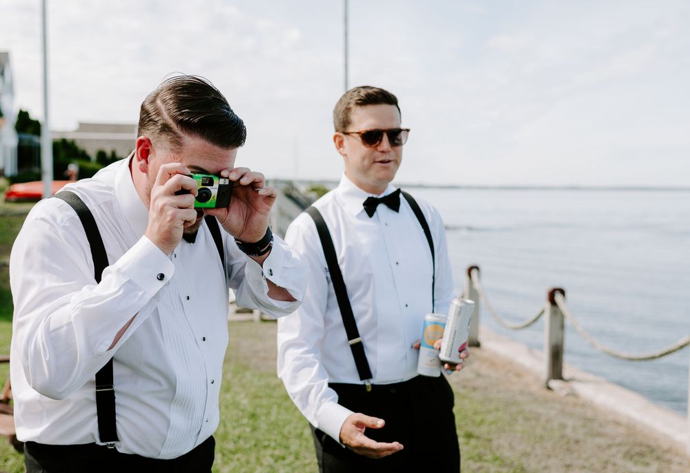 Groomsmen in suspenders and bowties drinking and celebrating outdoors.