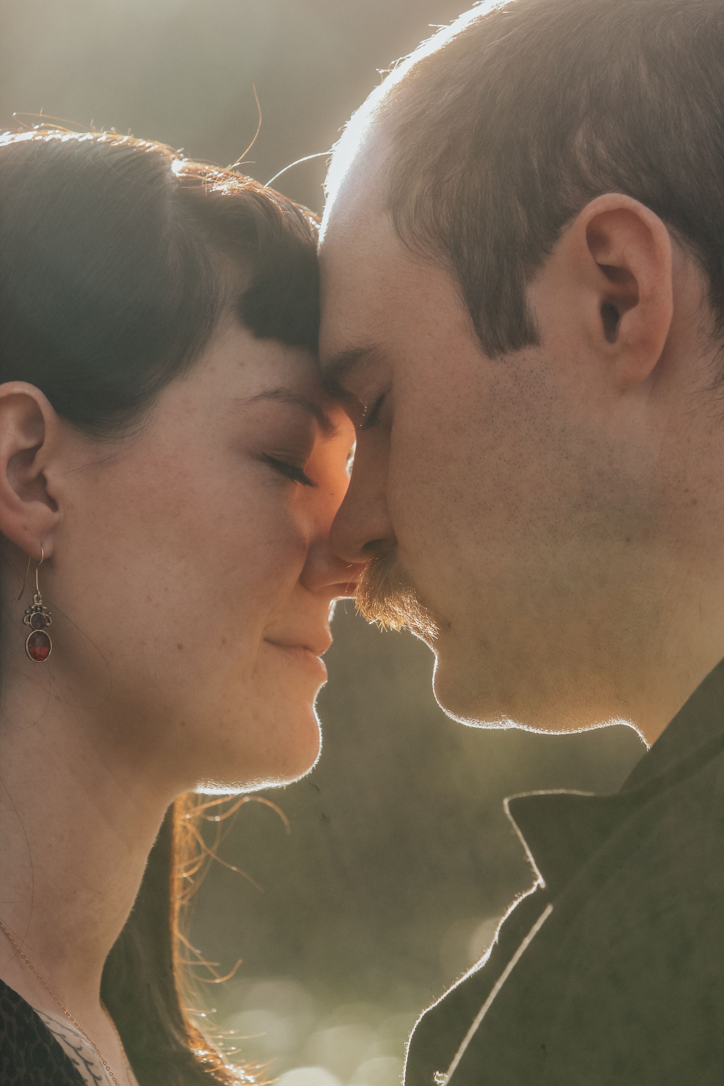 Intimate close-up portrait of couple touching foreheads in golden sunlight.