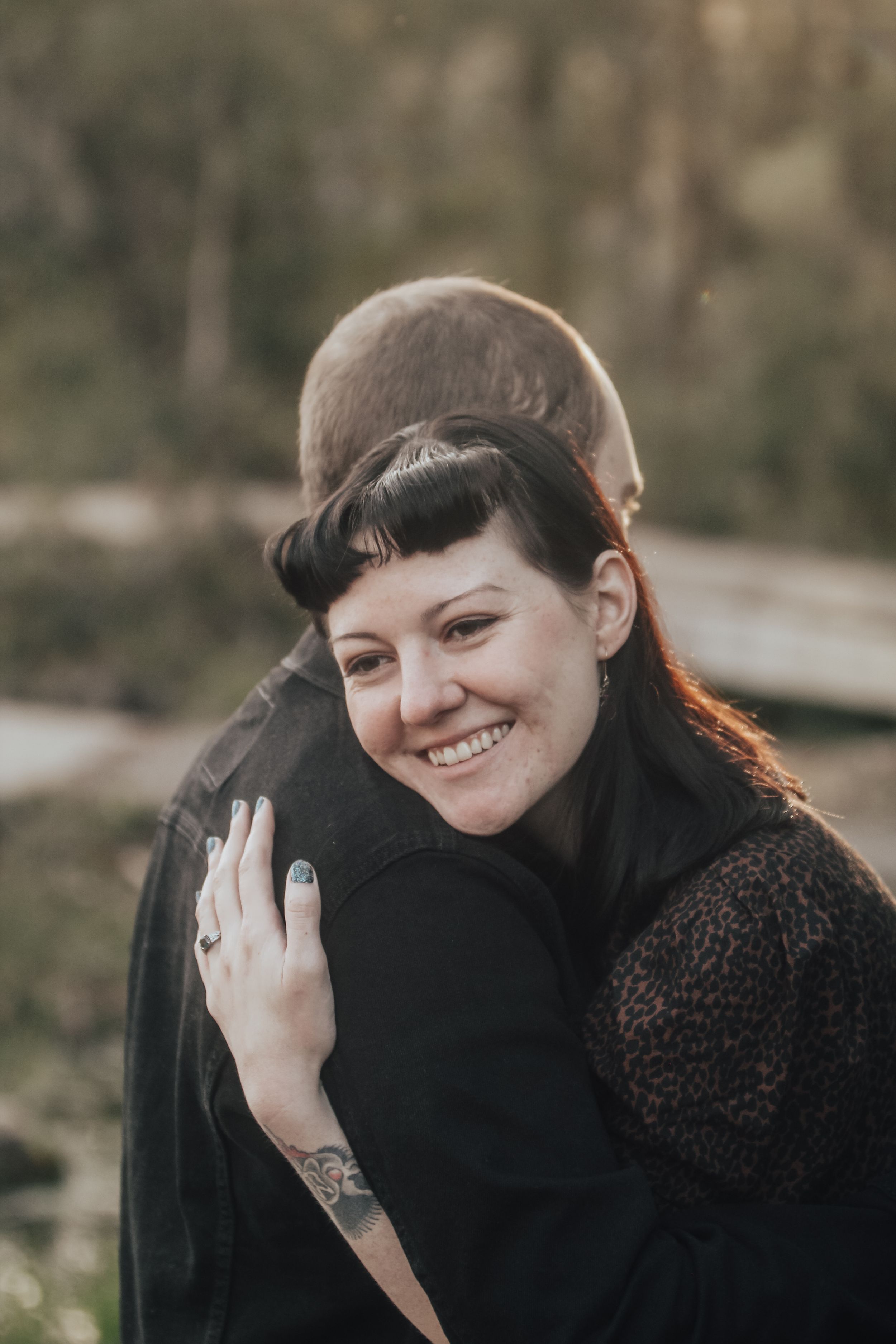 Close-up portrait of woman with bangs smiling warmly outdoors.