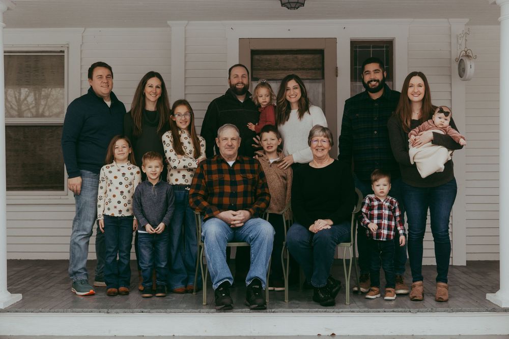 A group portrait of family members sitting and standing together on a front porch.
