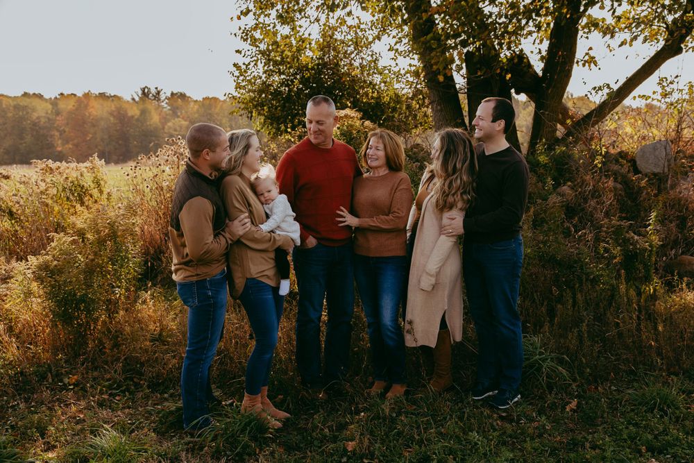 A group of people gather together outdoors in a golden autumn field during sunset, sharing warm laughter and conversation.