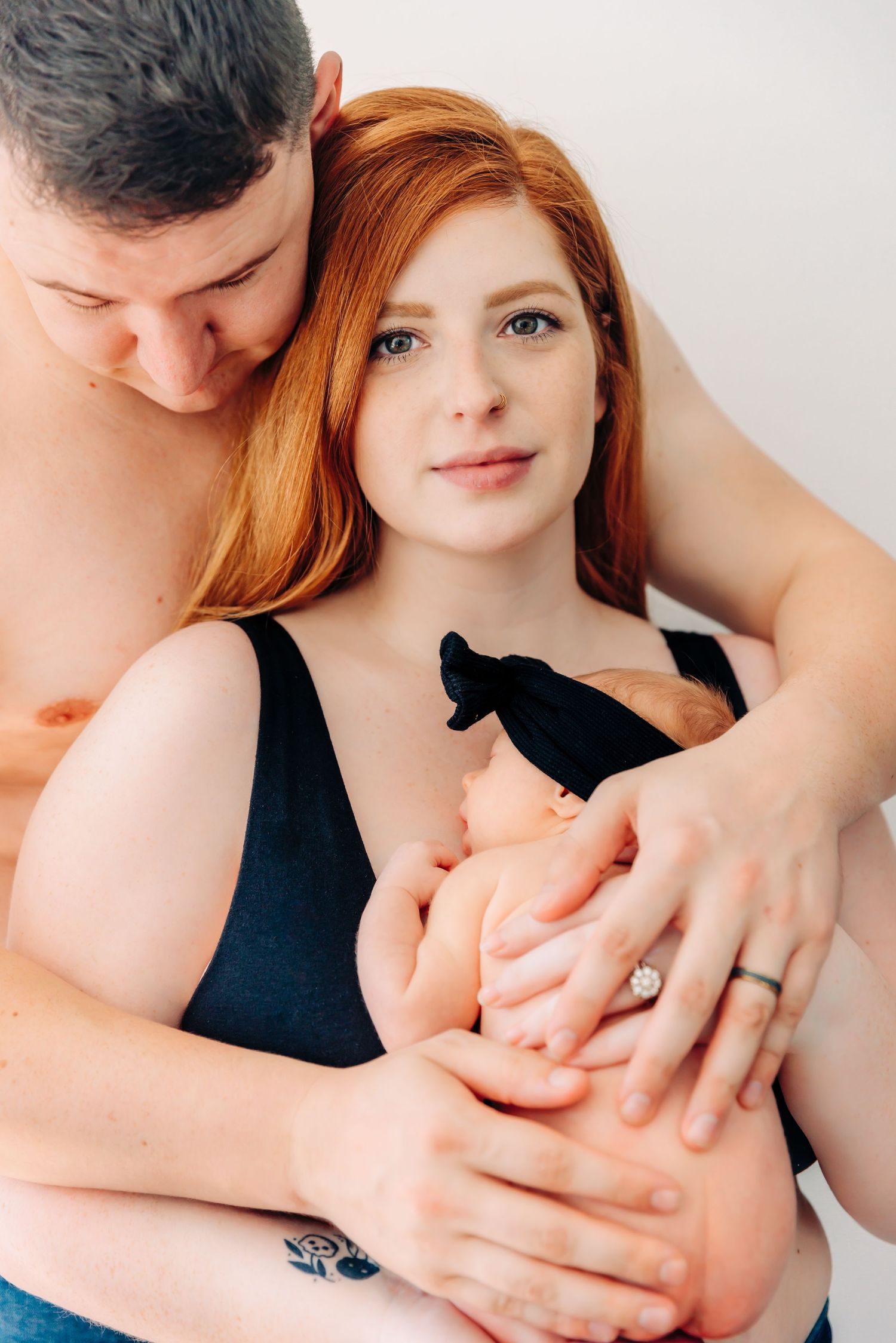 Family portrait with newborn wearing black bow against white background.