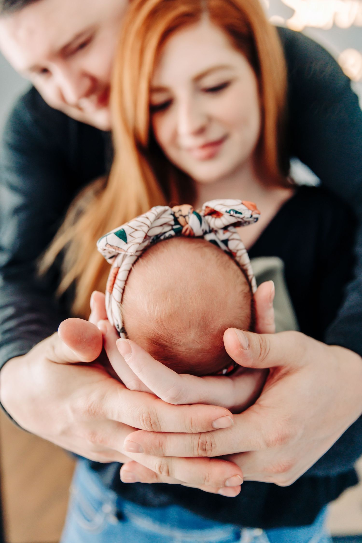 Parents holding their newborn baby's head adorned with a floral headband.