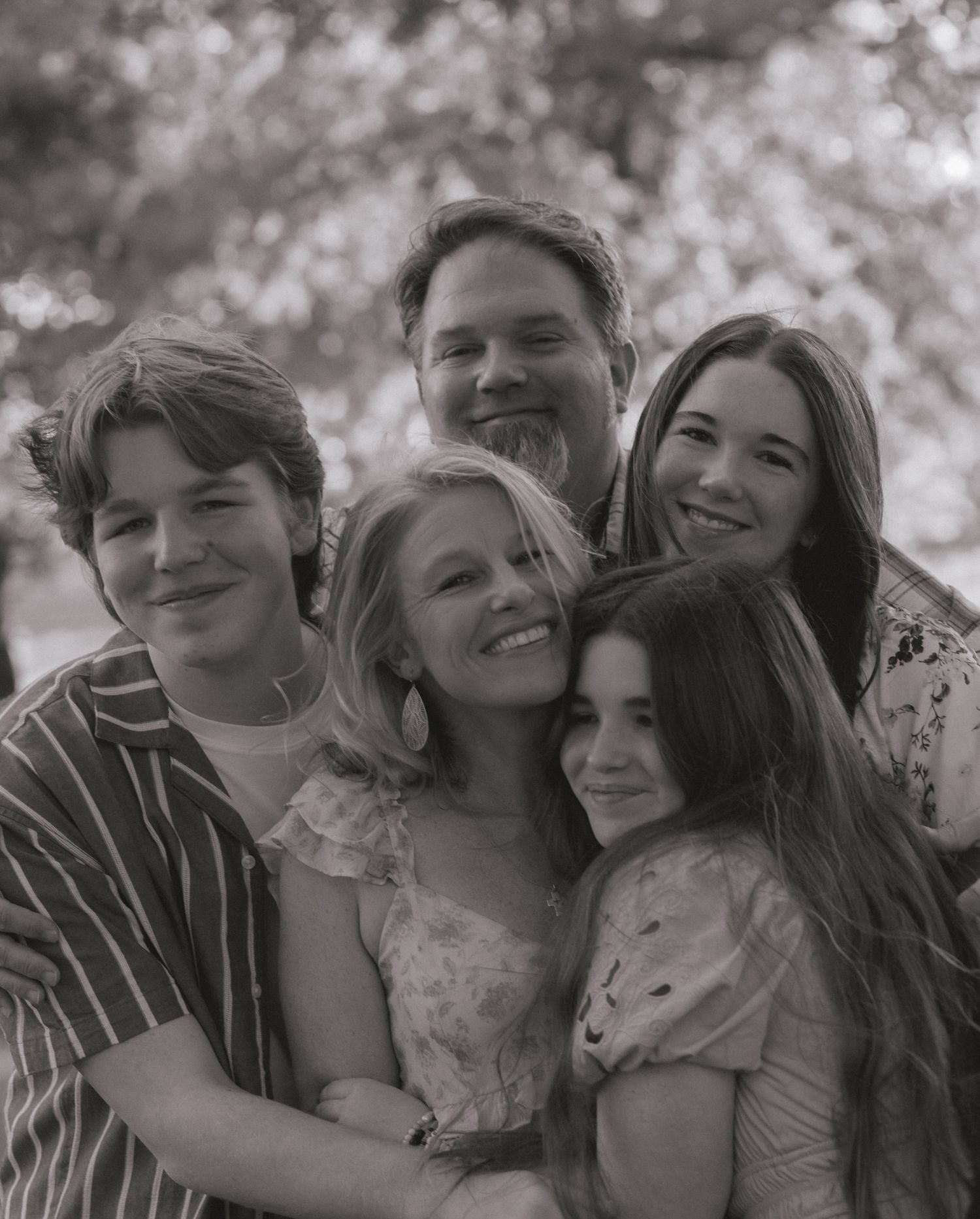 Happy family of five sharing a warm embrace, captured in classic black and white photography.