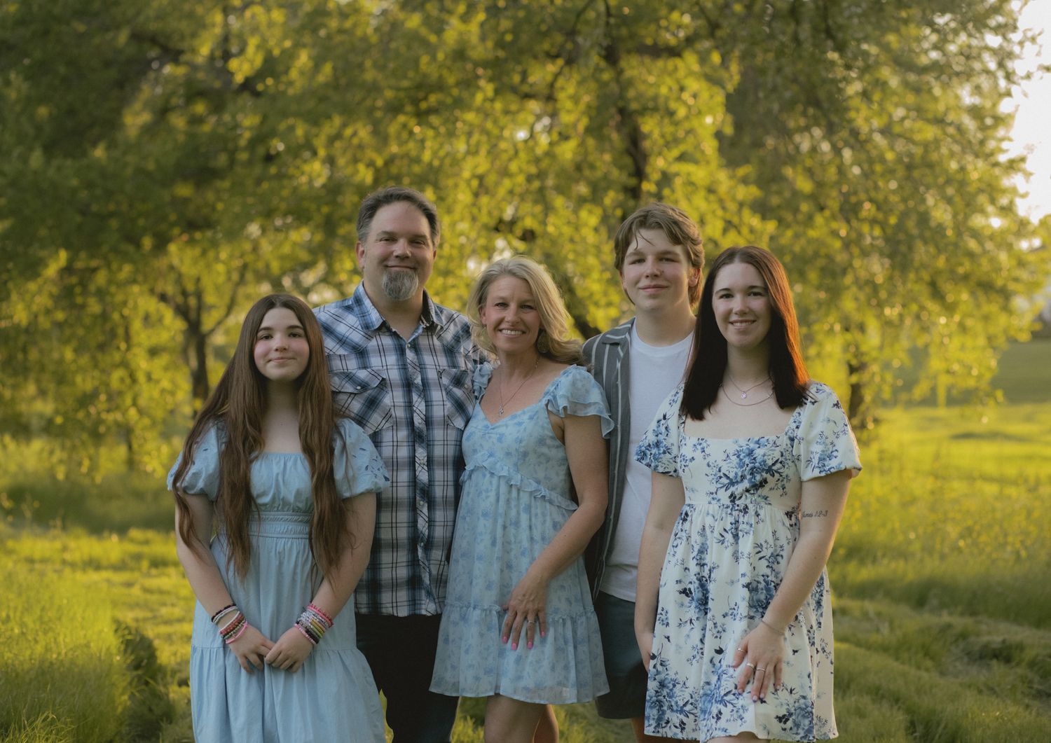 Family of five posing together in a sunlit green park during golden hour photography session.