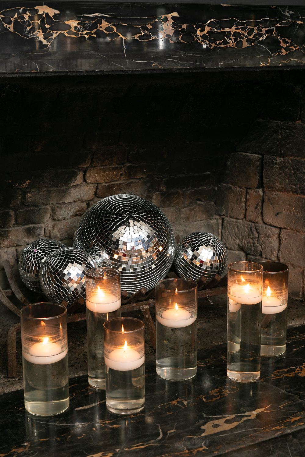 Glowing disco balls and floating candles in glass cylinders create a moody atmosphere against an old fireplace