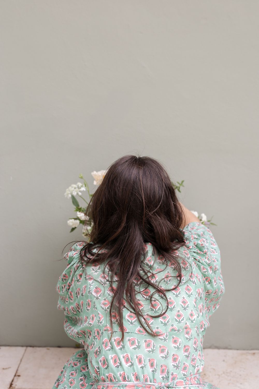 A person with long dark hair in a mint and pink floral dress laying down arranging a bouquet of flowers