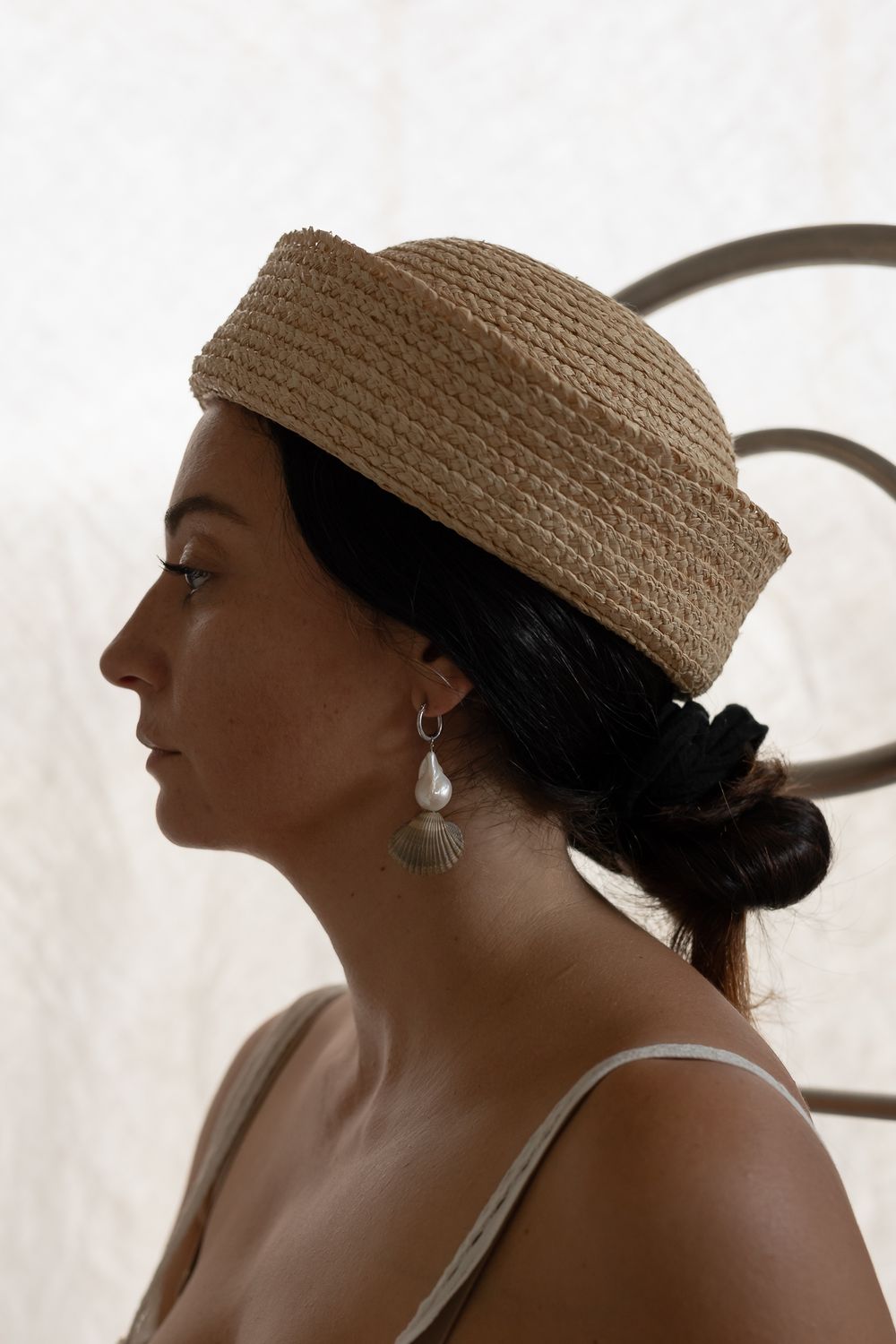 Woman in profile wearing a woven straw hat and shell earrings with dark hair in a bun.