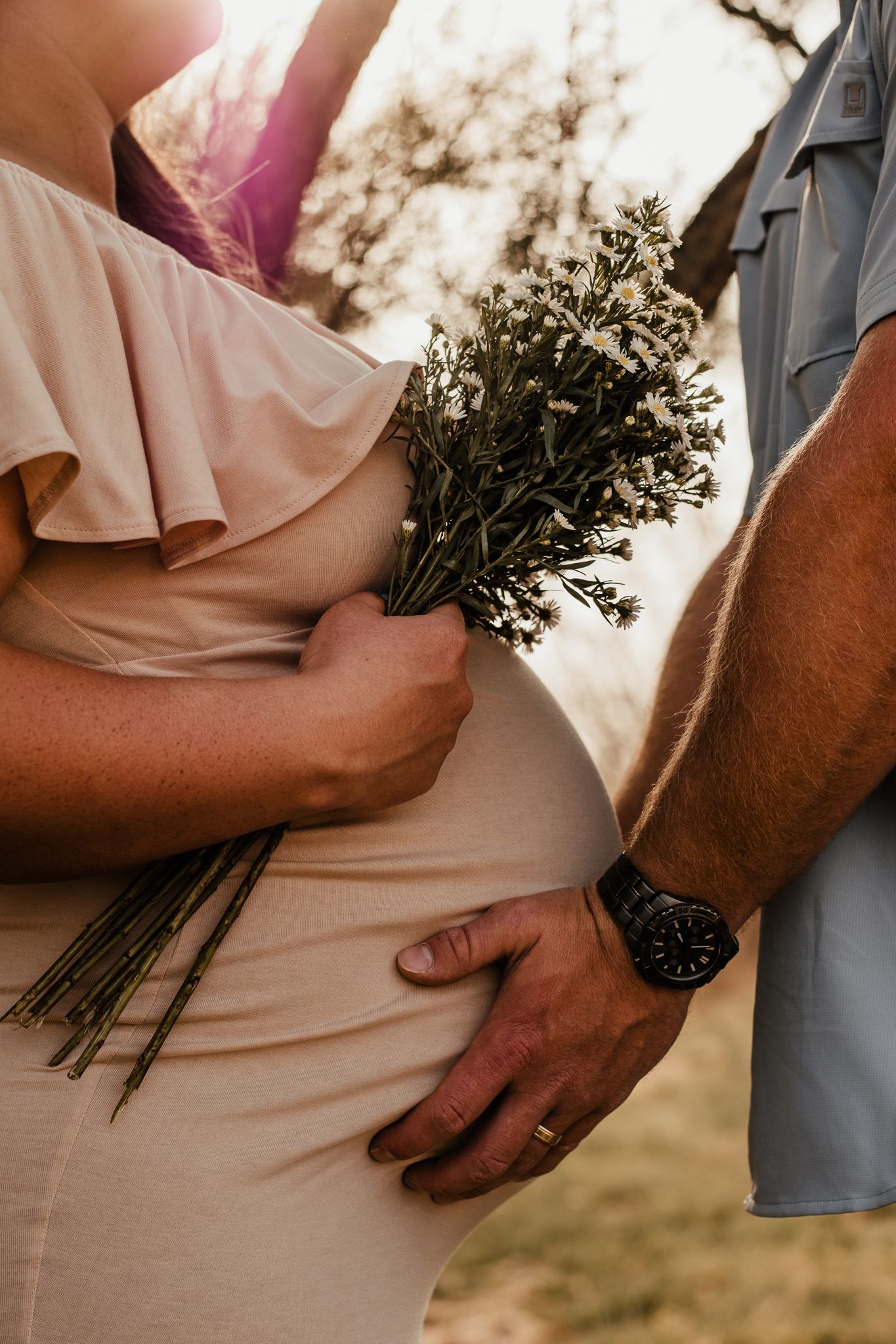 A maternity photo featuring dried flowers and intimate moment between couple at sunset.