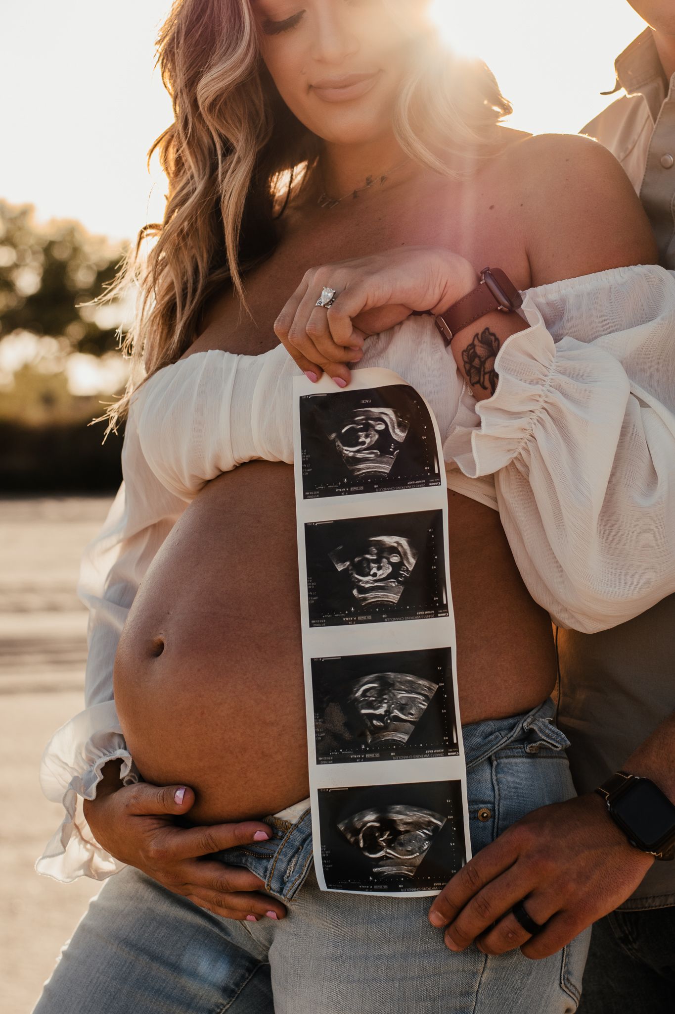 A strip of ultrasound photos being held against a pregnant belly in warm sunlight.