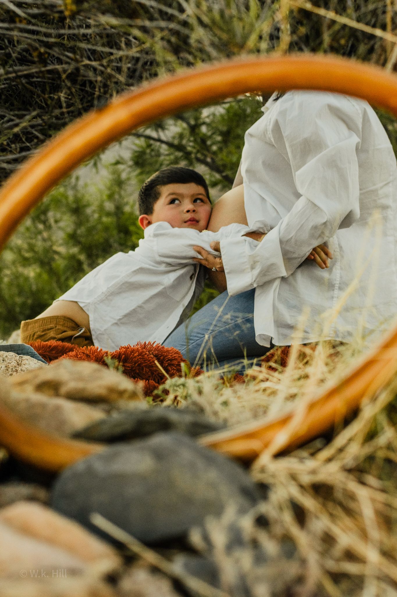 A mirror reflection captures a toddler playing in grass and rocks outdoors.