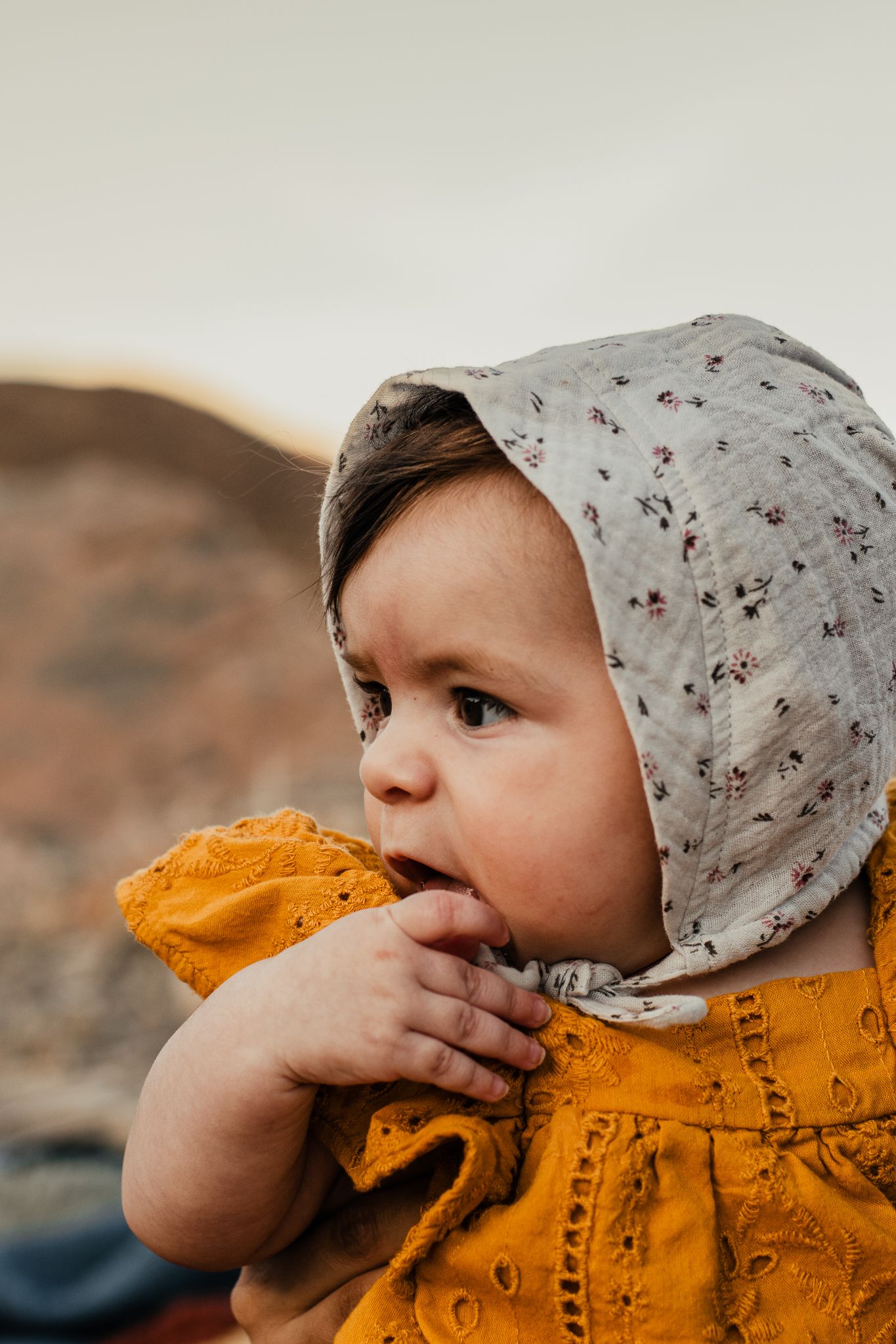 A small child in an orange dress and floral bonnet looking to the side.