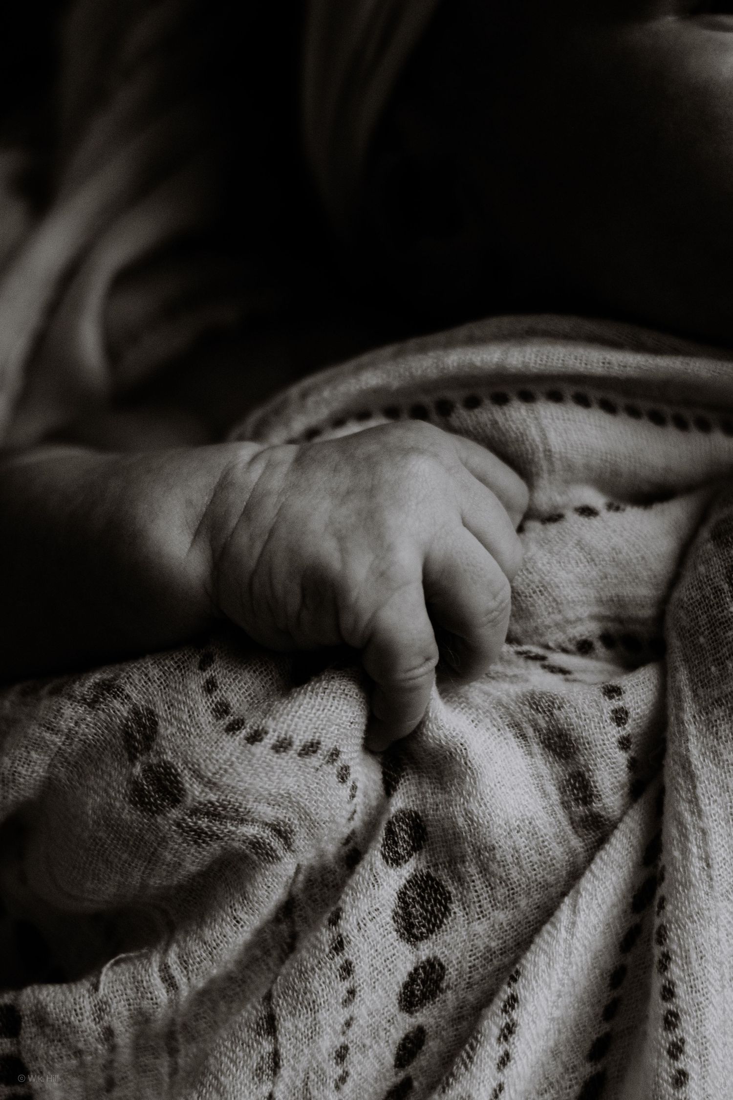 Close up black and white photo of a baby's hand resting on a textured blanket.