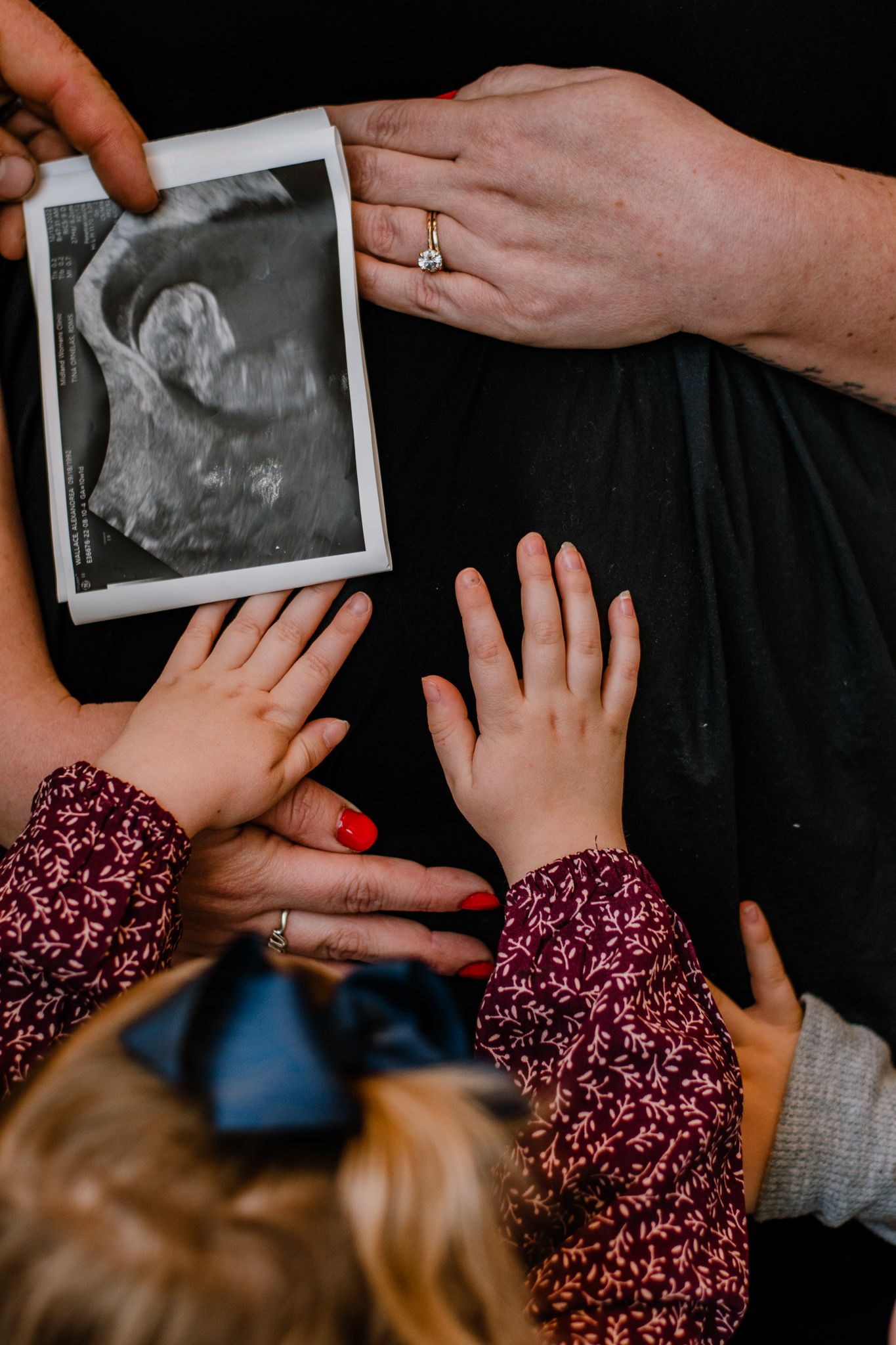 Hands holding an ultrasound photo with small children's hands reaching up to touch it.
