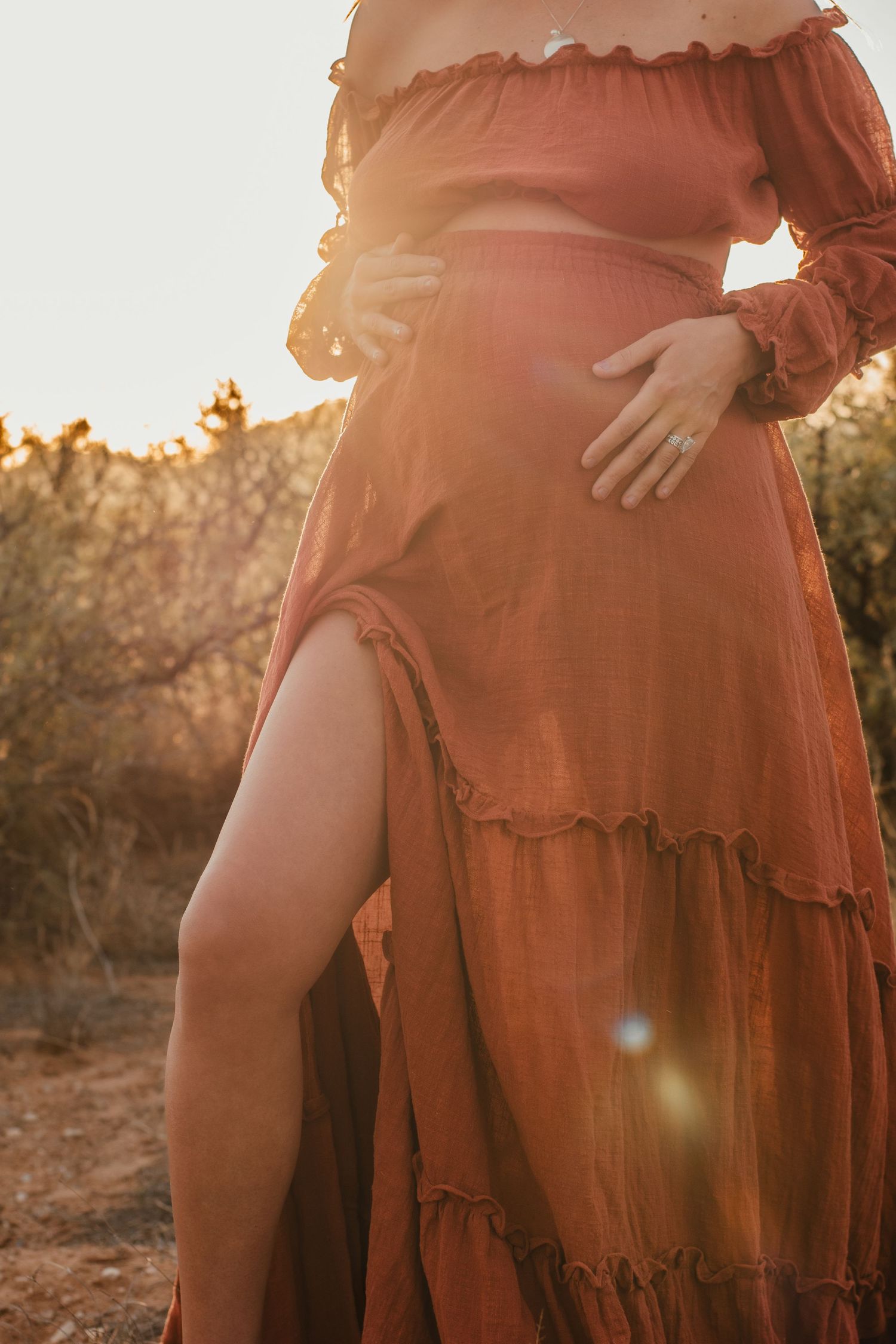 Close-up of a flowing rust-colored dress with ruffled details in sunset lighting.