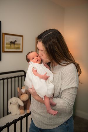 Tender moment between parent and newborn baby in nursery with gray walls.