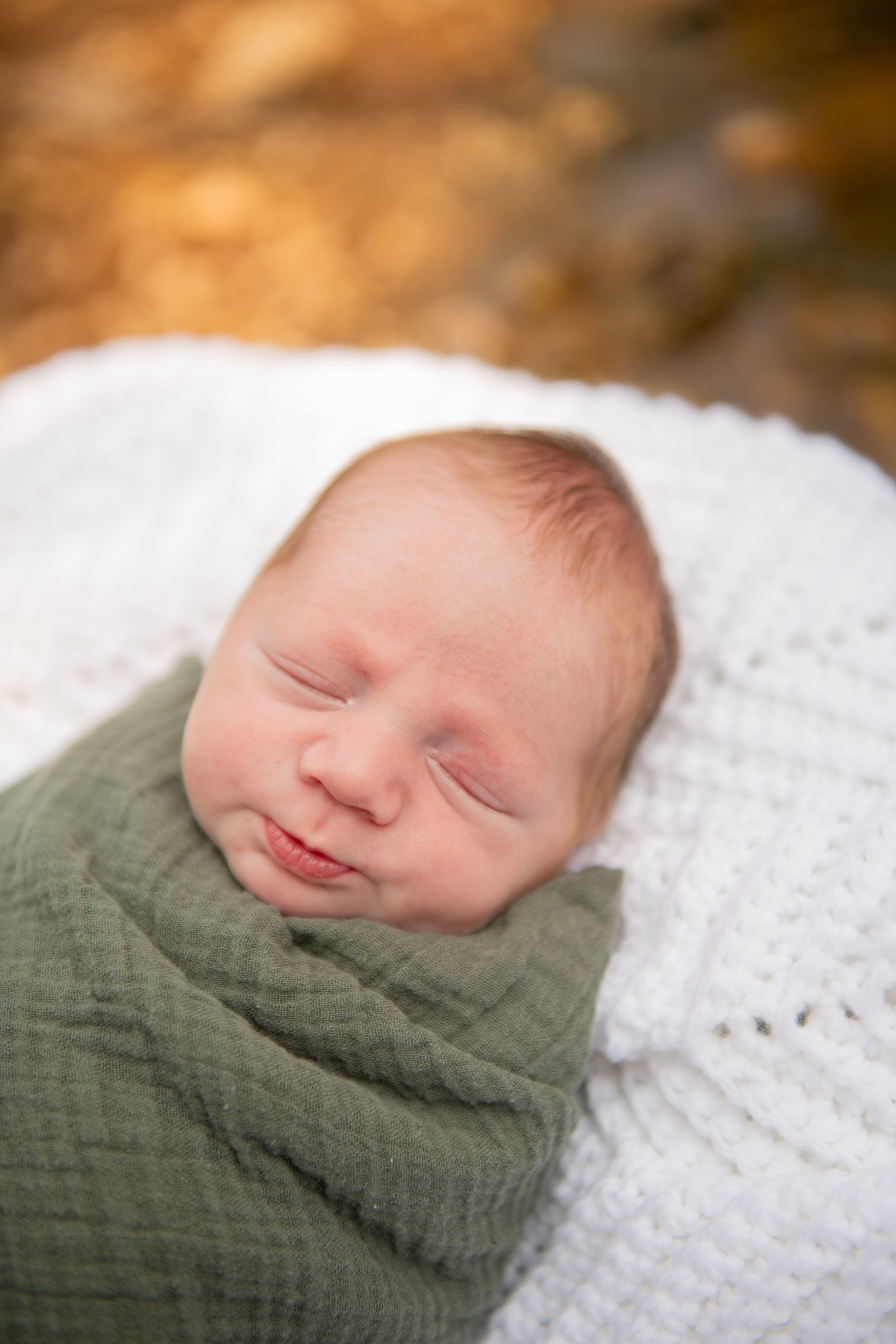 Newborn baby sleeping peacefully swaddled in a soft green wrap on white blanket.