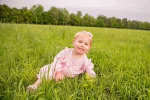 Baby in pink outfit crawling through tall green grass on sunny day.