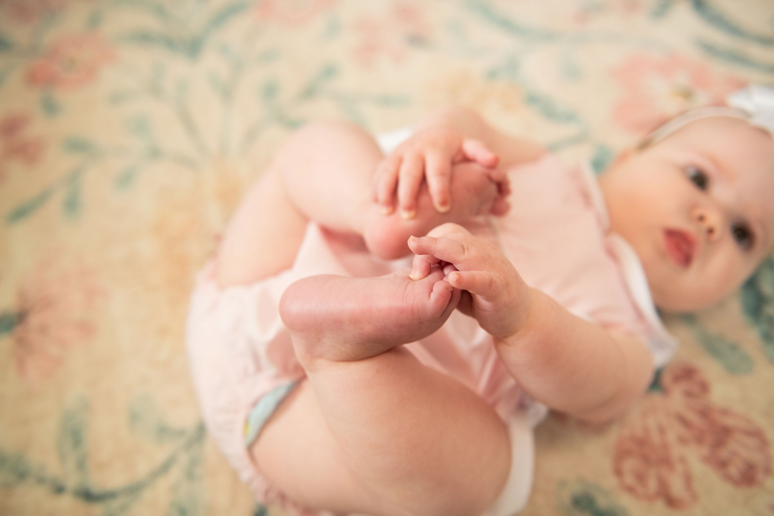 Close-up details of baby's tiny hands against floral pattern background.