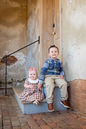 Two children sitting on brick steps against weathered wall with rustic railing.