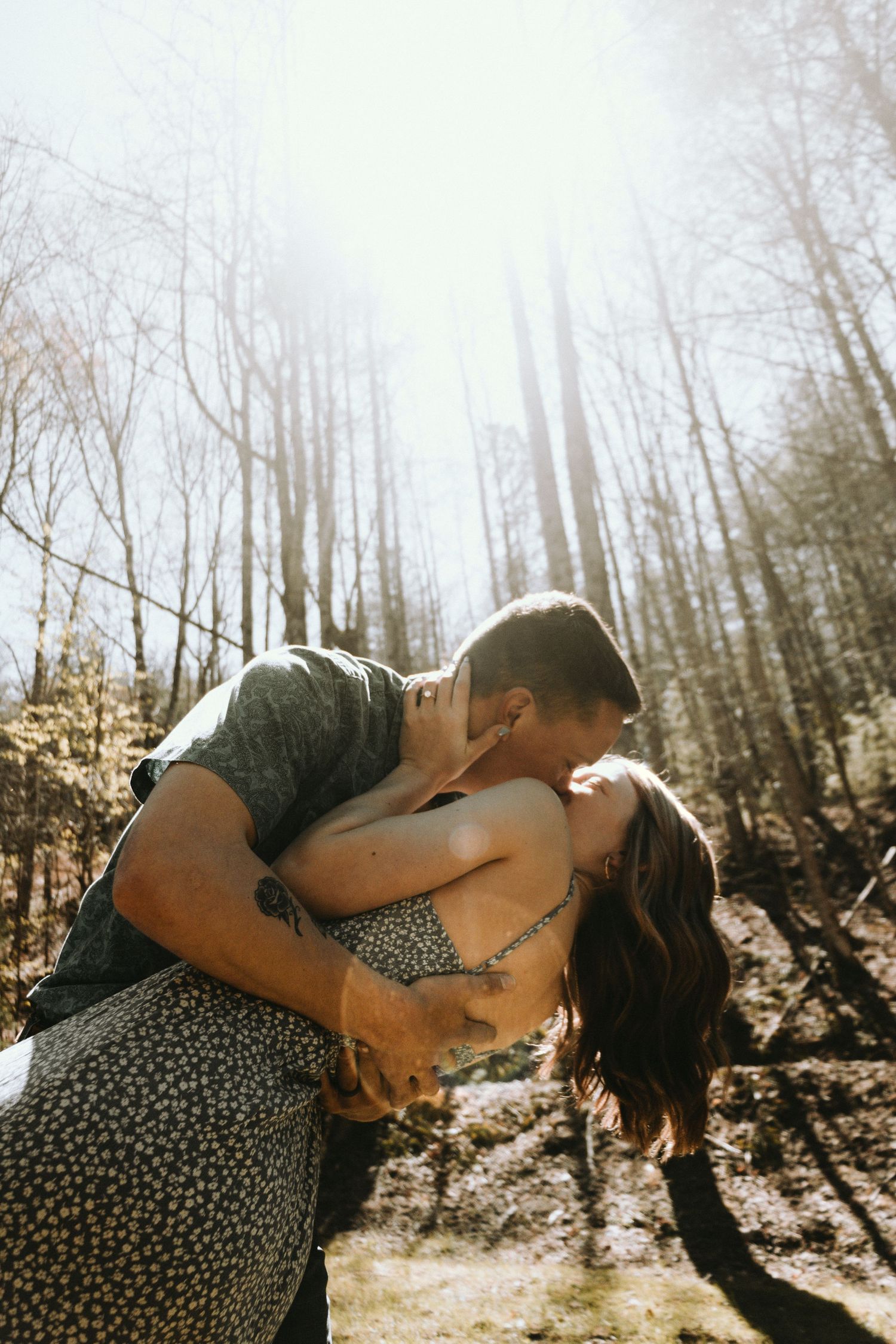 Romantic dip kiss in sunlit forest clearing.