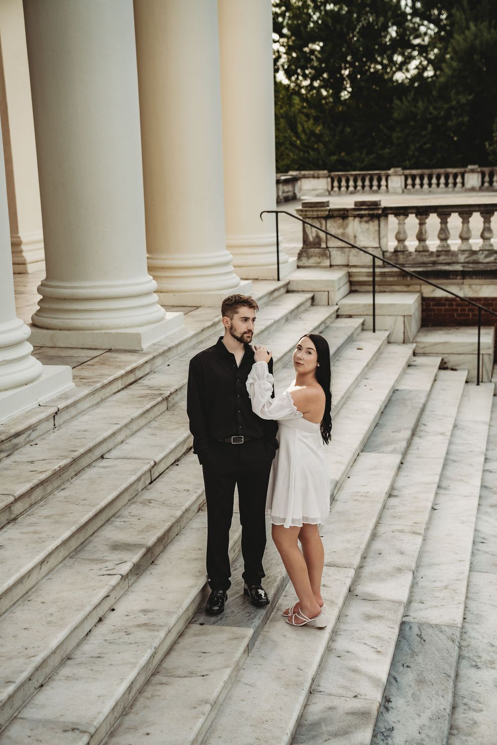A couple shares romantic moments on white stone steps with elegant columns in the background.