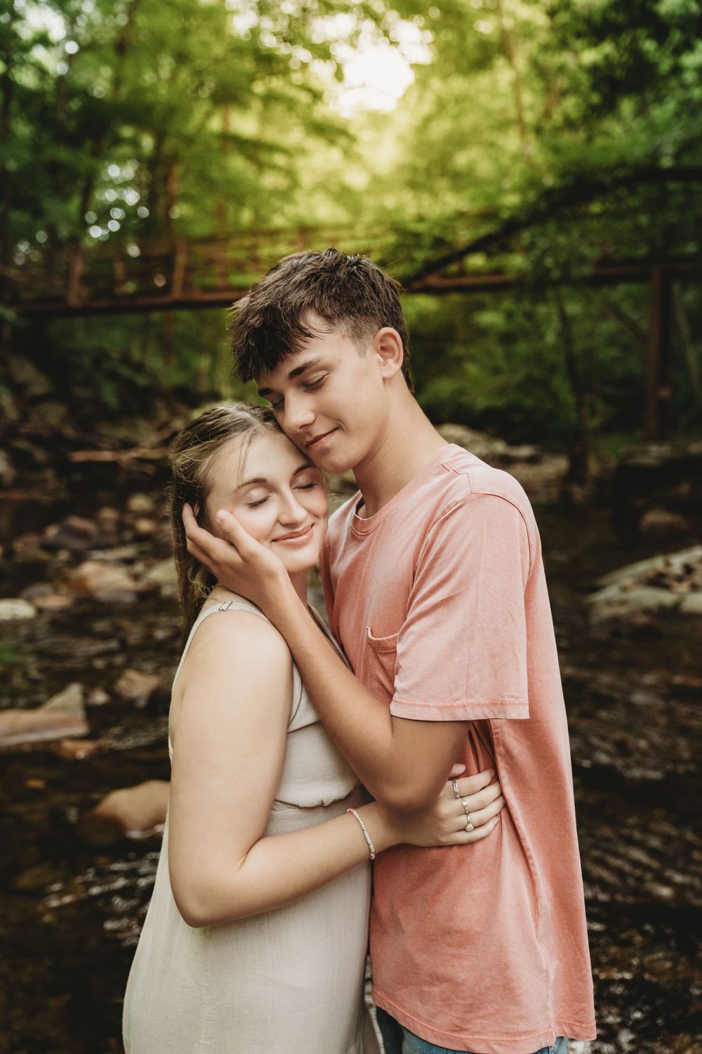 A tender moment captured in nature showing a warm embrace between two people in a wooded setting.