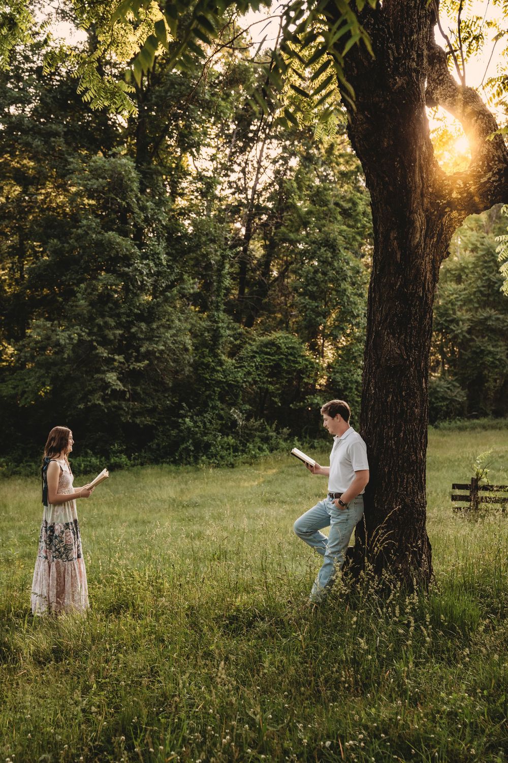 Couple reading vows apart in golden sunset meadow by large tree.