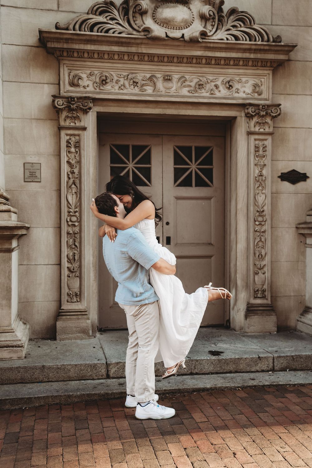 A romantic embrace in front of an ornate stone doorway with decorative carvings and brick pavement.