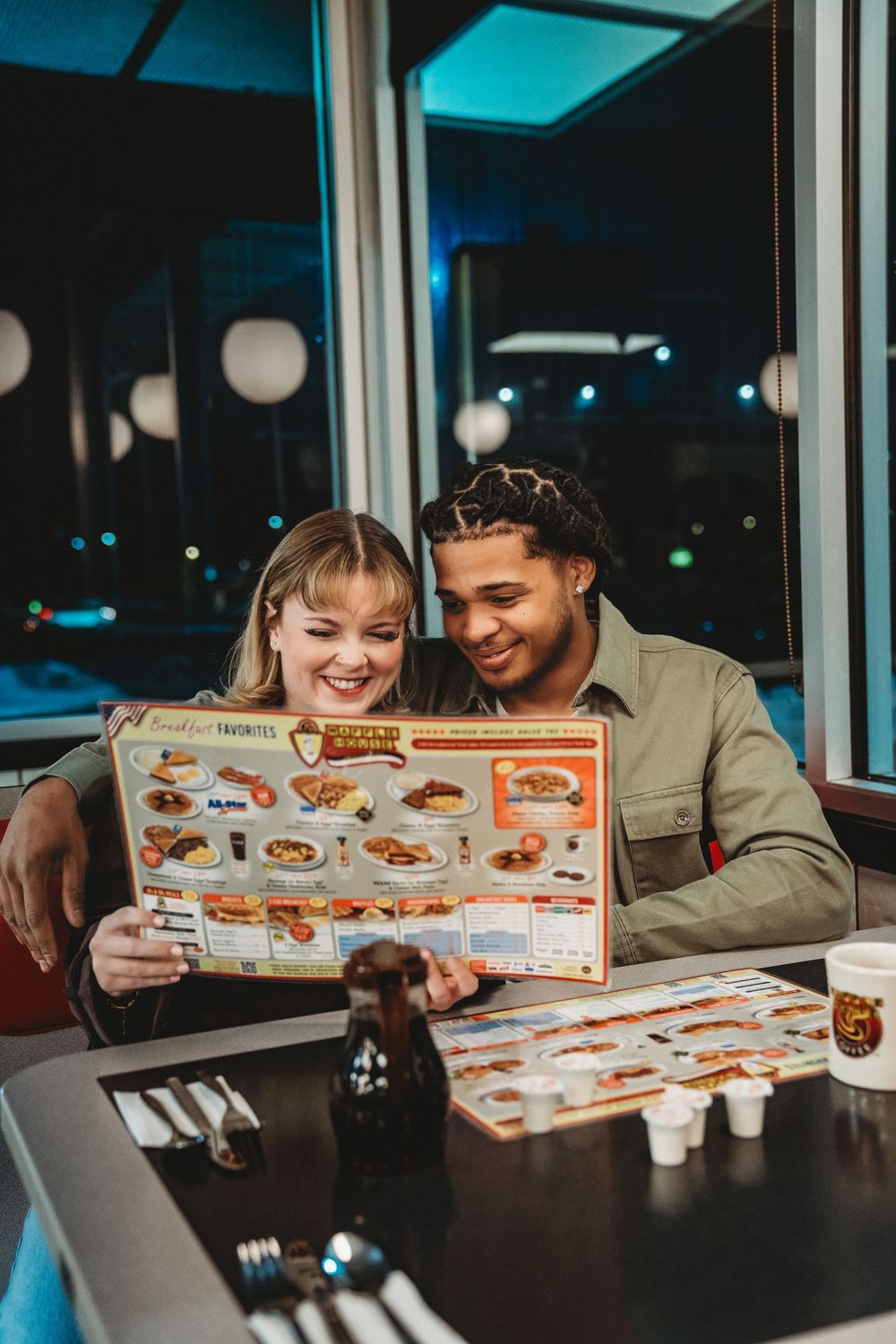 Two people sitting at a restaurant table looking at menus together and smiling in blue ambient lighting.