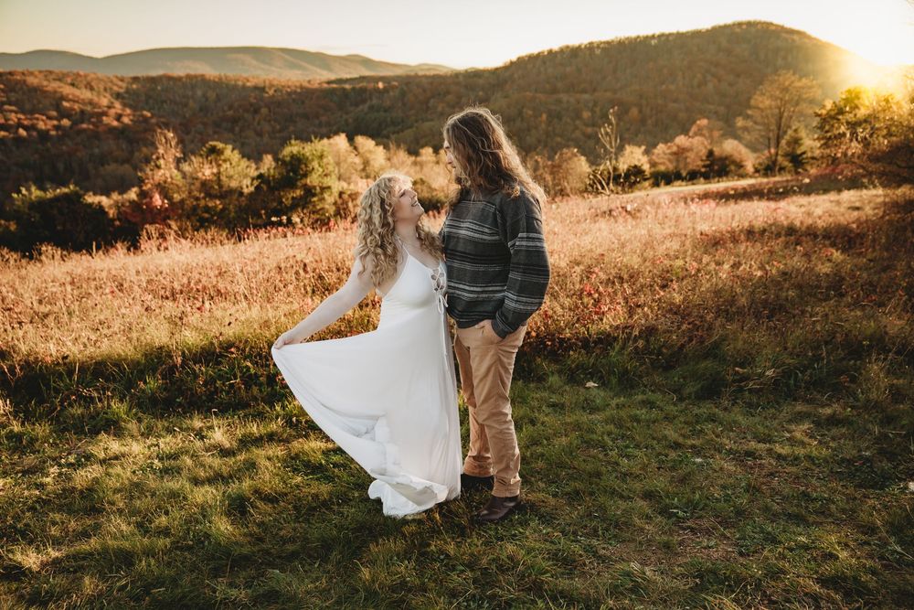 Couple dancing at golden hour sunset in a scenic mountain meadow, bride in white dress twirling with groom in rustic attire.