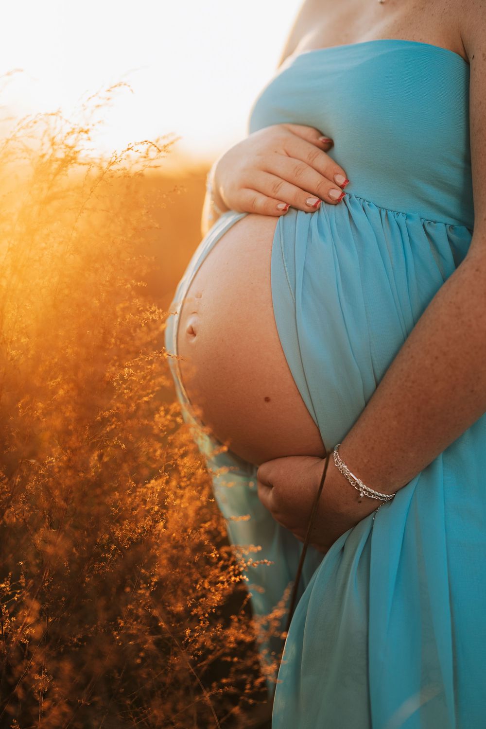 A series of maternity photos showing a pregnant belly in a turquoise dress against a warm sunset glow through trees.