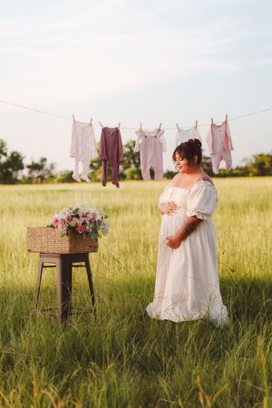 Pink and white baby clothes hanging on a clothesline in a serene meadow with golden evening sunlight.