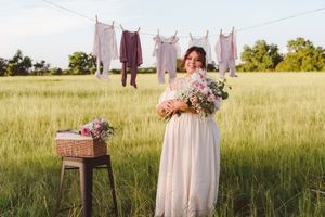 A clothesline displays vintage garments and linens against a green meadow with flowers at sunset.