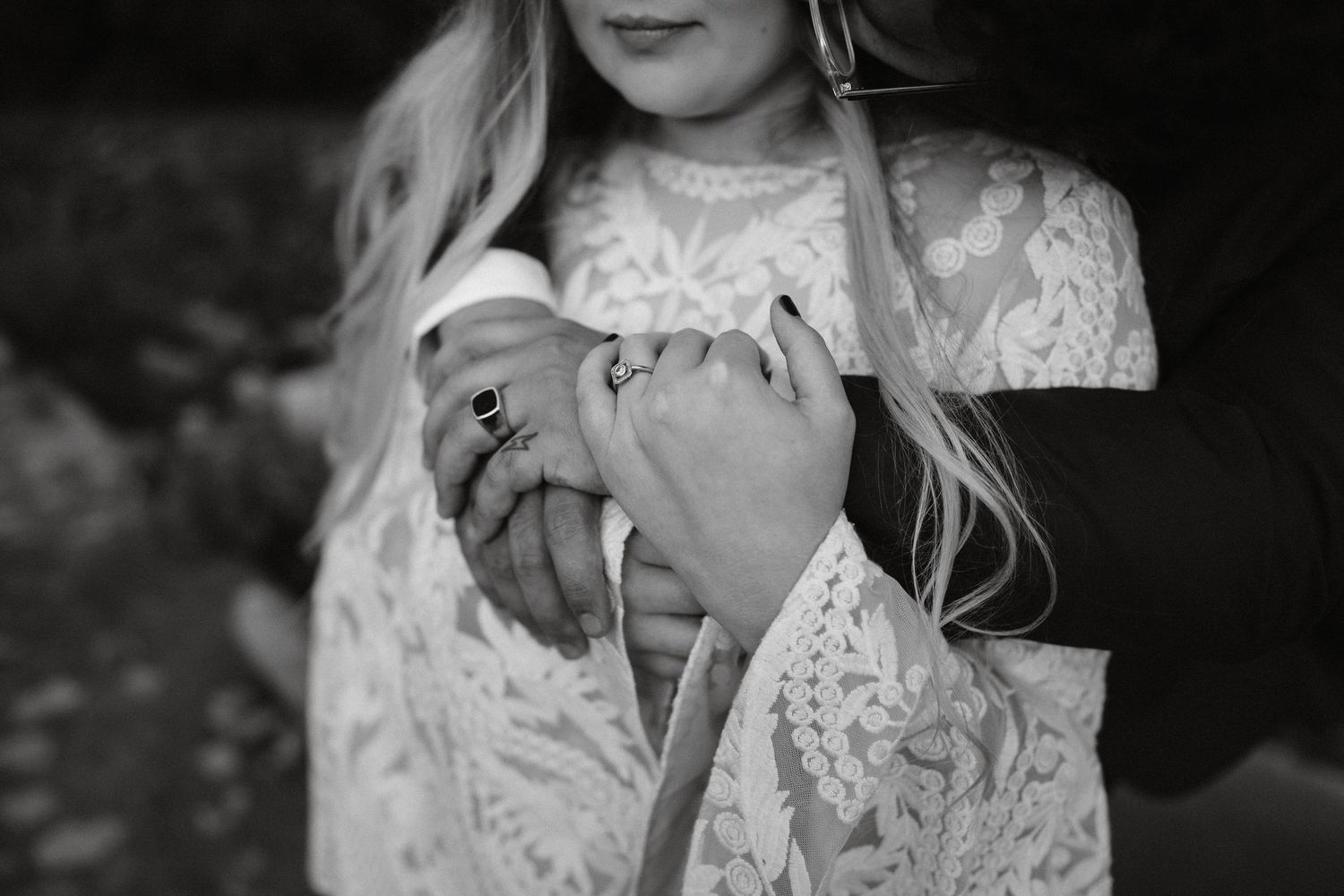 Bride in lace dress smiles with eyes closed in sunlit outdoor setting.