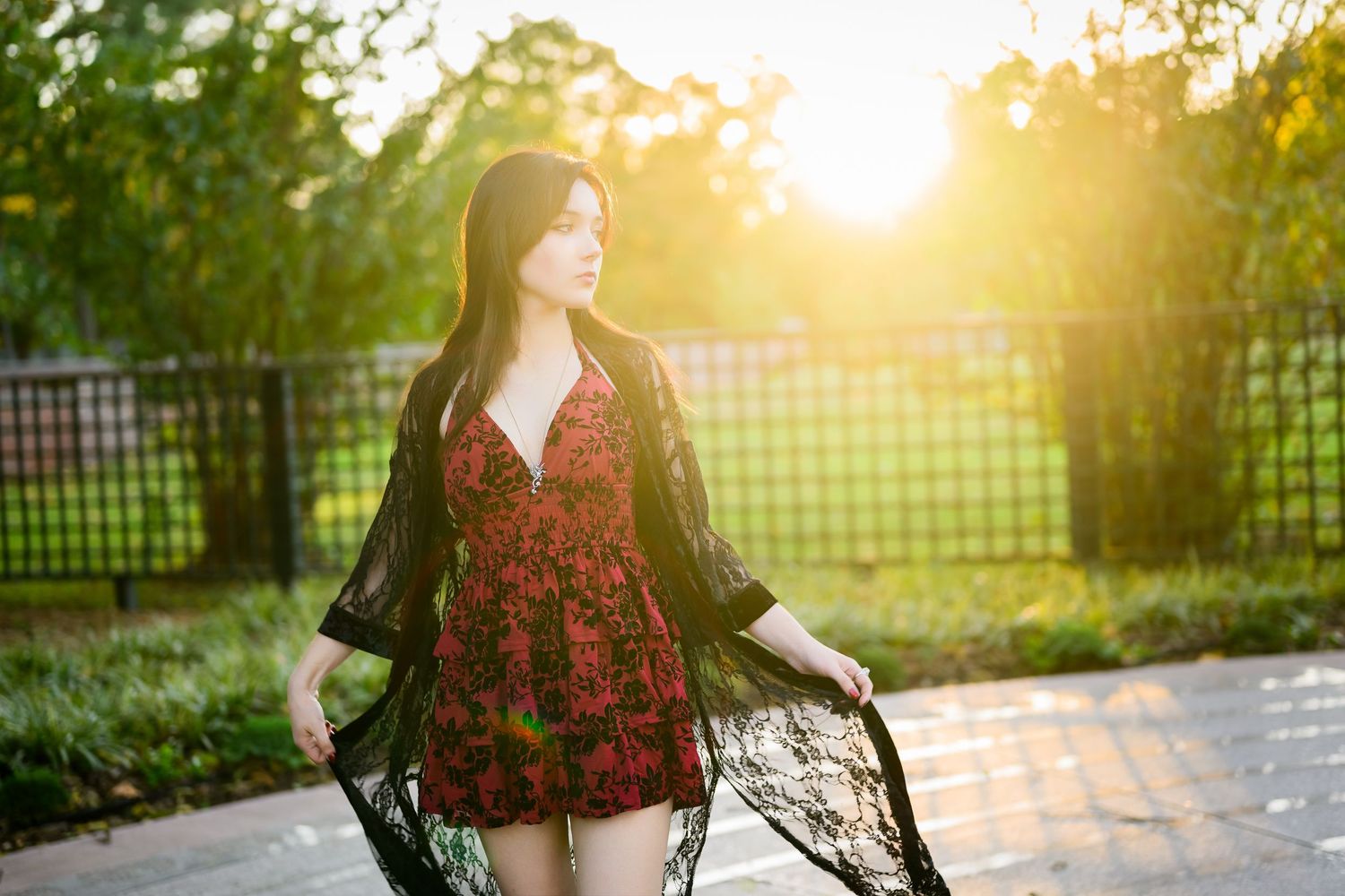 Person in red floral dress poses outdoors during golden hour sunset with dreamy backlit lighting.