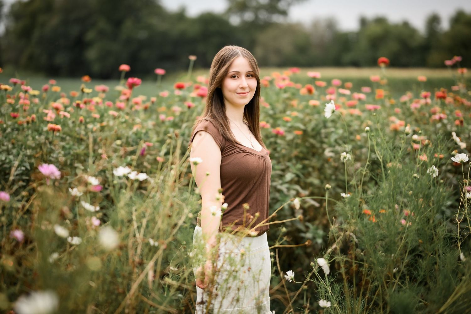 A person stands in a vibrant field of orange and pink wildflowers on a sunny summer day.