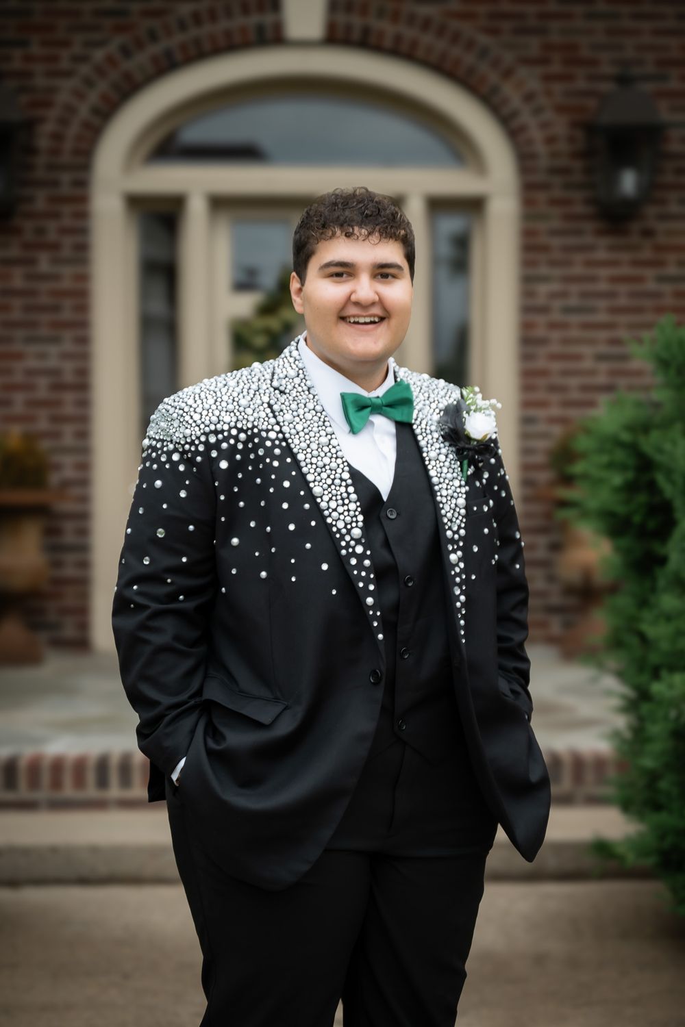A formal black tuxedo with a green bowtie and unique white scattered dot pattern stands before a brick entrance.