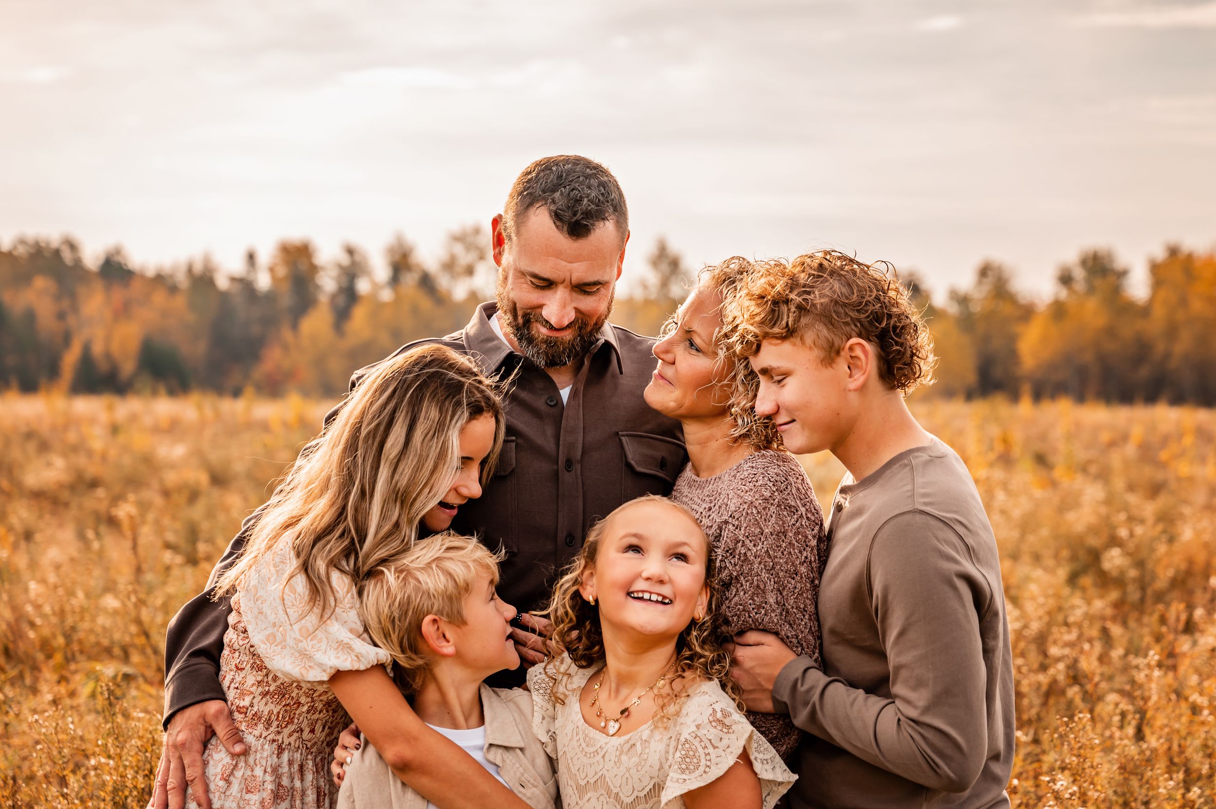 A family shares tender moments together in a golden autumn field during sunset.