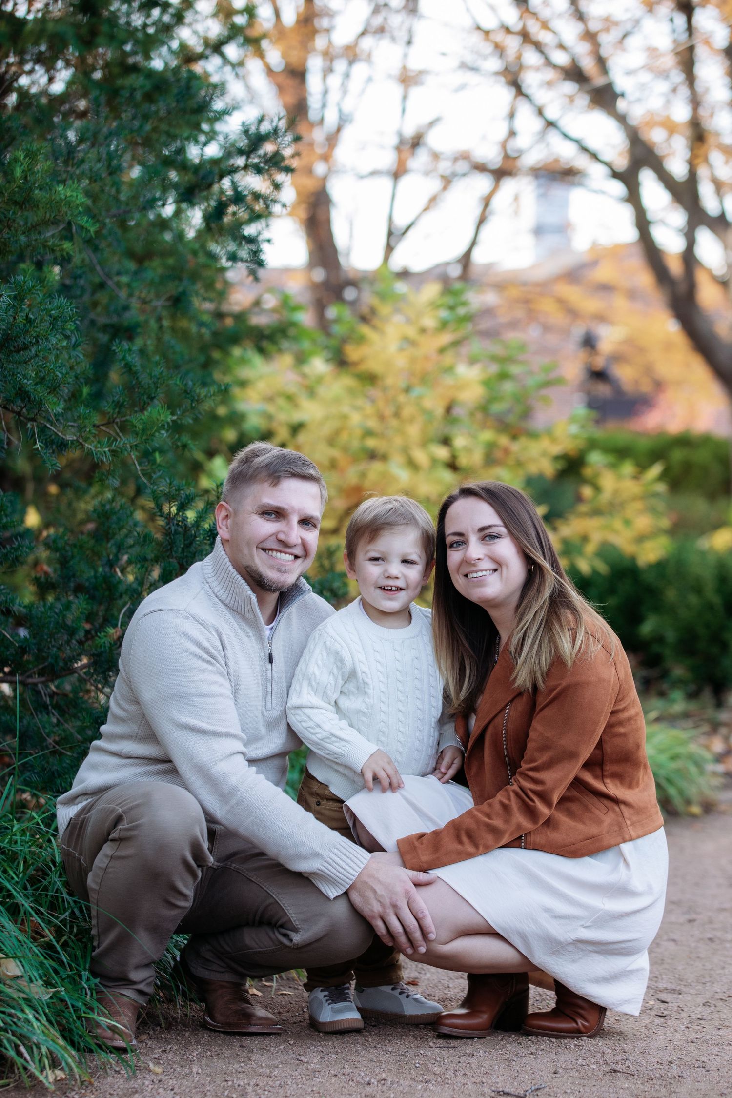 A family in coordinated fall outfits poses together on a garden path during an autumn photoshoot.