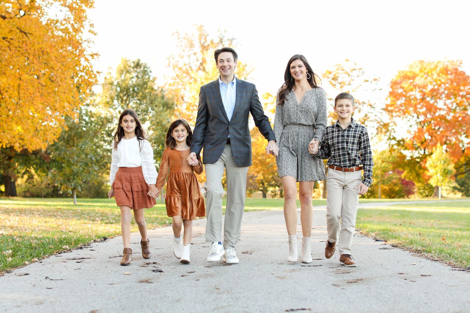 Family walking together on path surrounded by fall trees with golden leaves.
