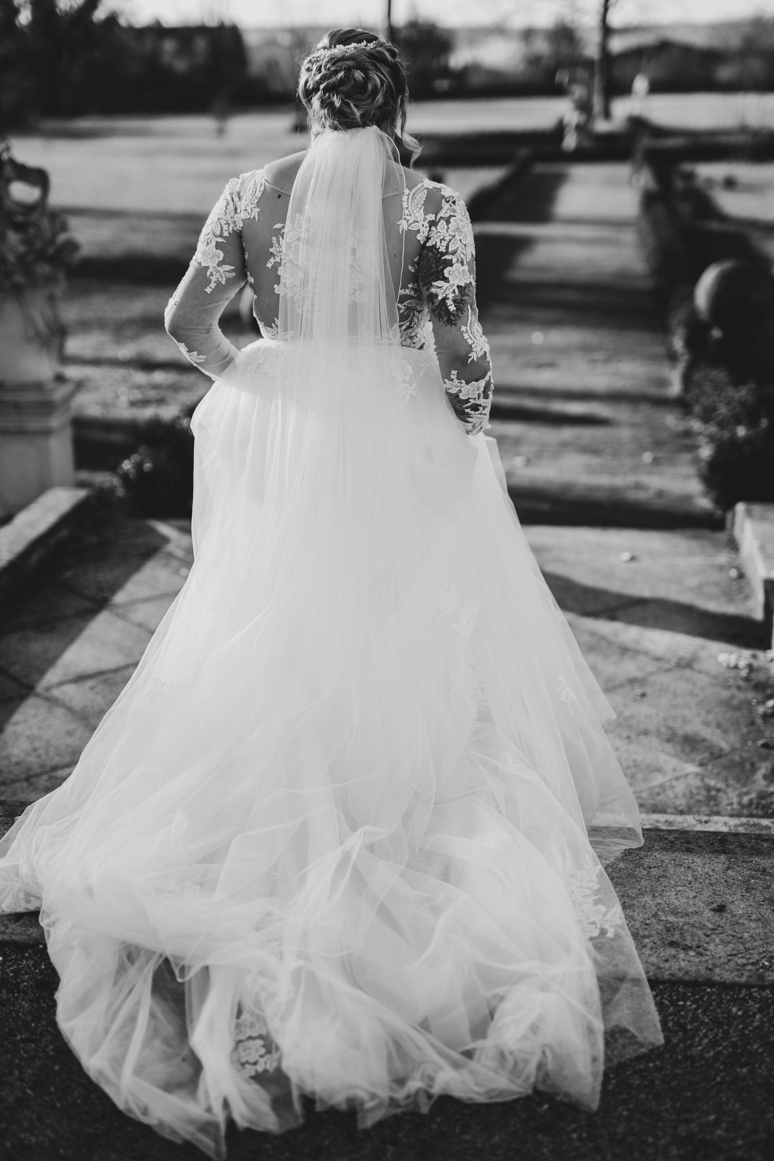 Black and white photo of flowing wedding dress trailing behind on outdoor path.
