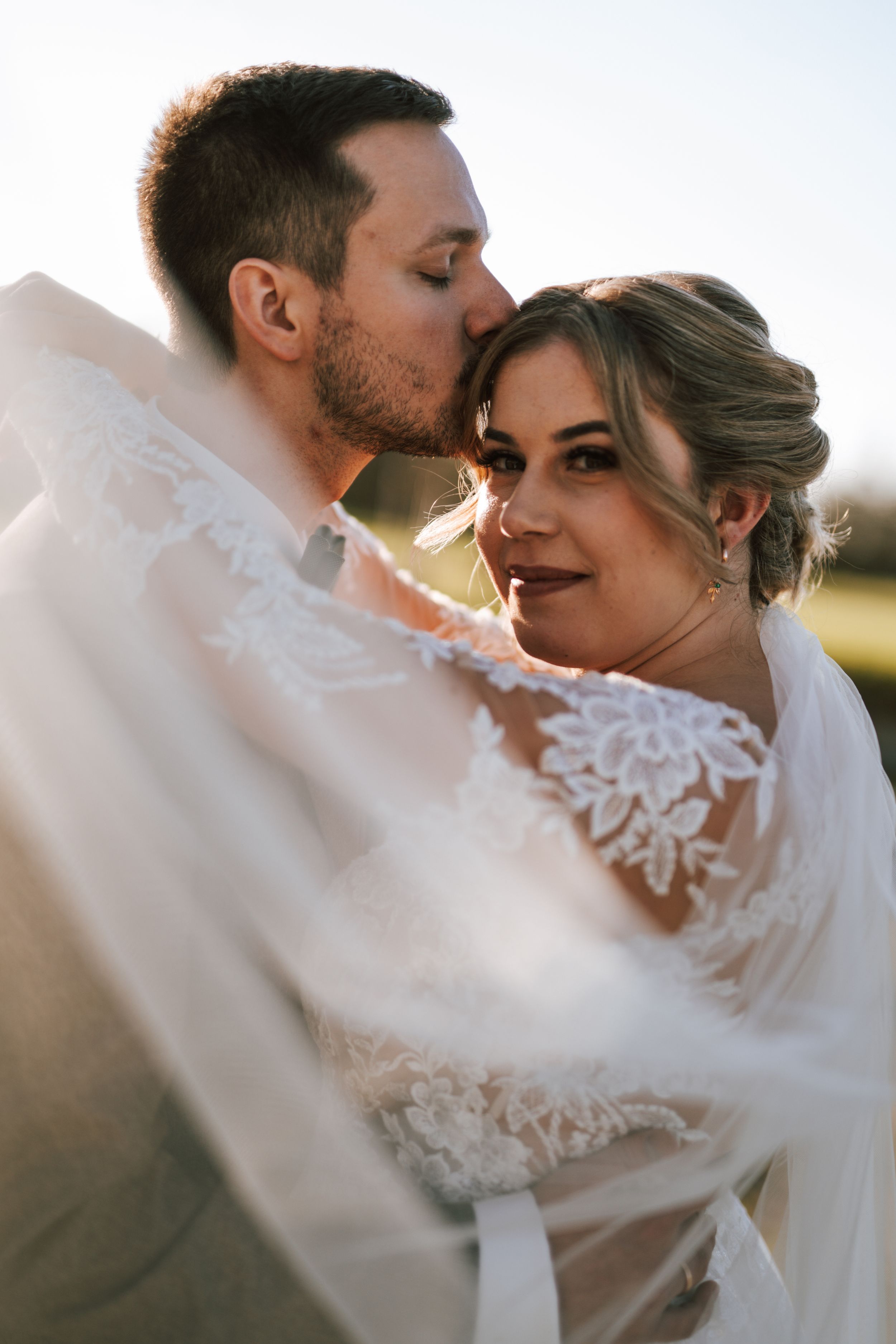 Intimate wedding portrait with flowing veil captured in golden hour light.