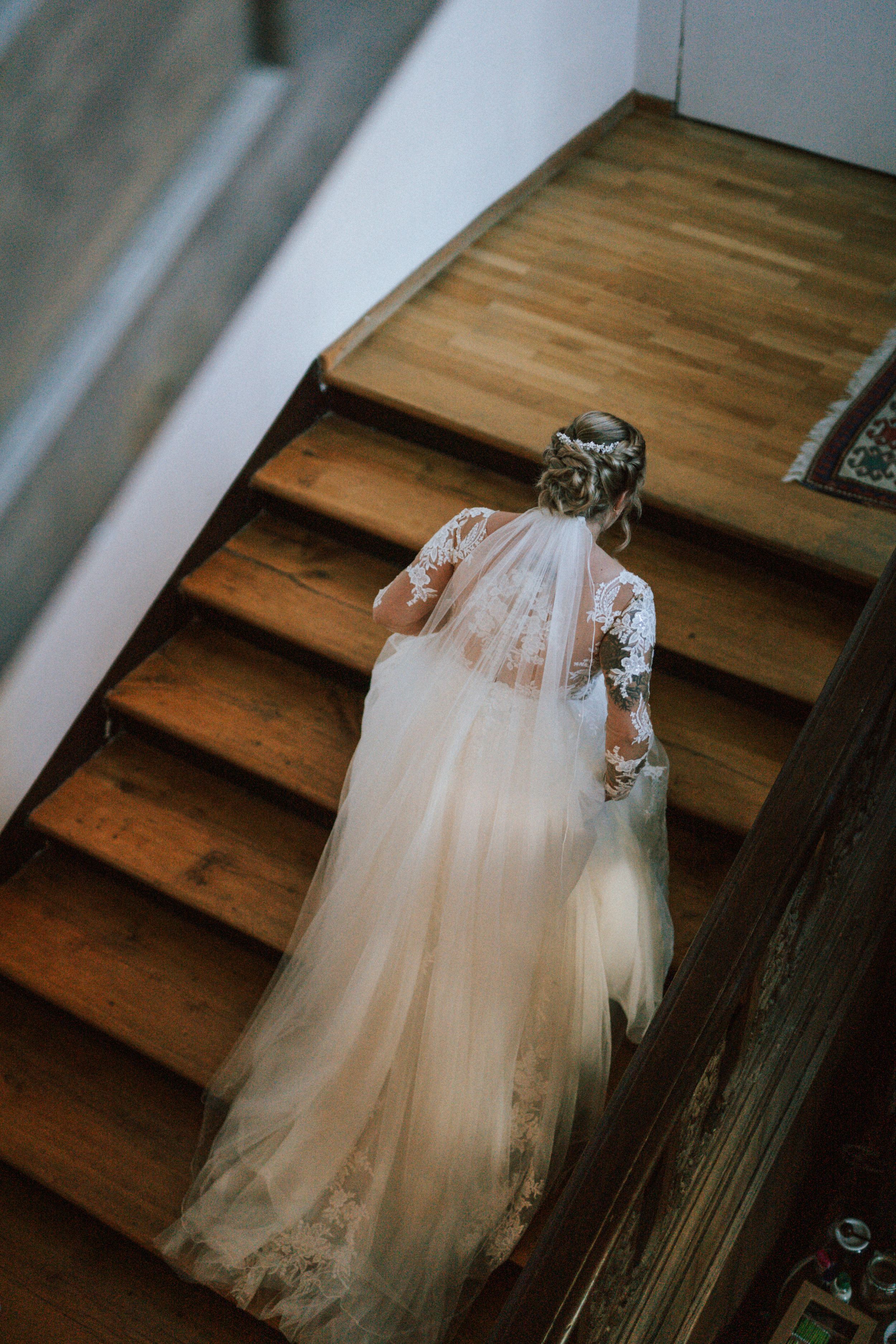 Wedding dress with tulle skirt cascading down wooden stairs in natural light.