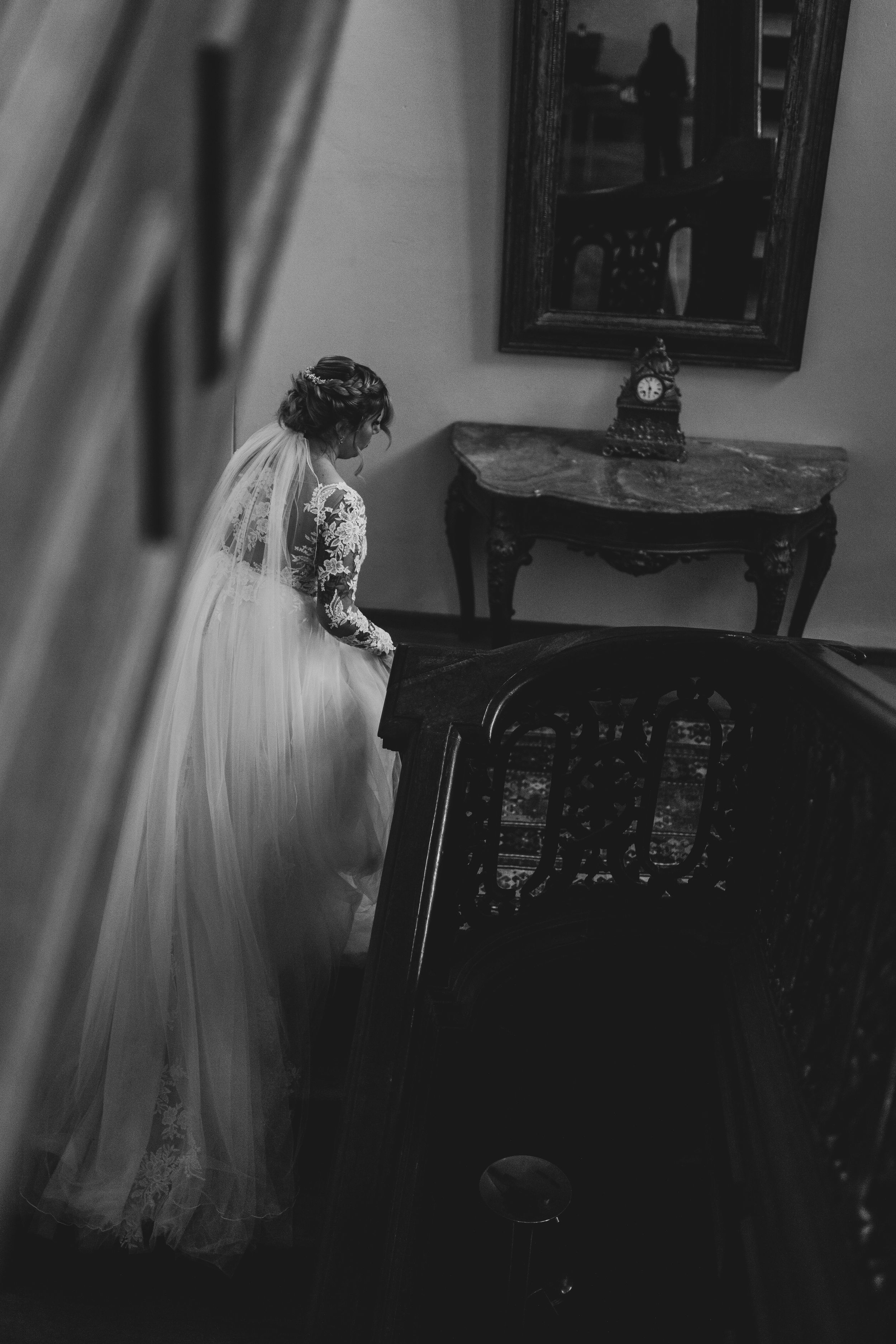 A bride in a flowing white dress stands beside a piano in a dimly lit room creating a moody atmosphere.