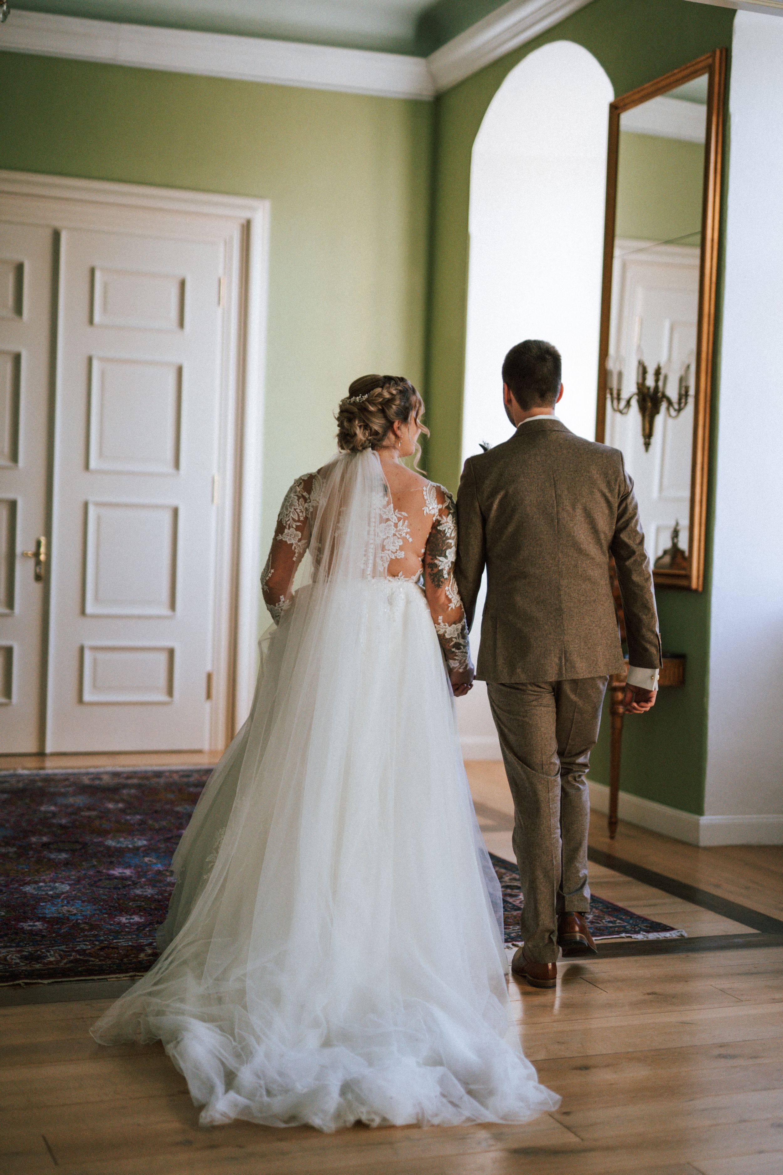 Wedding couple walking through elegant green-walled hallway with white trim.