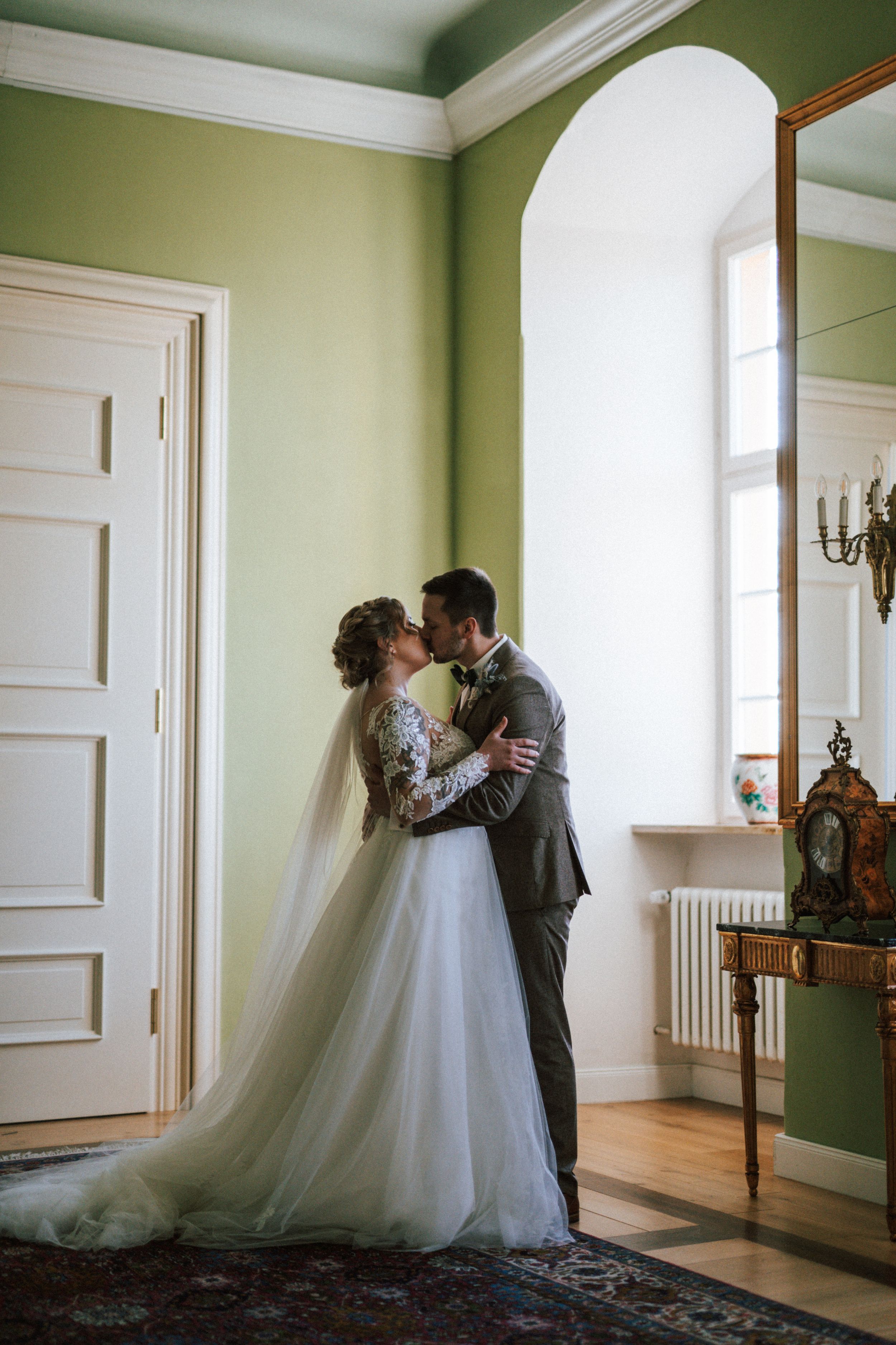 Intimate wedding couple moment in sunlit green room with classic architectural details.