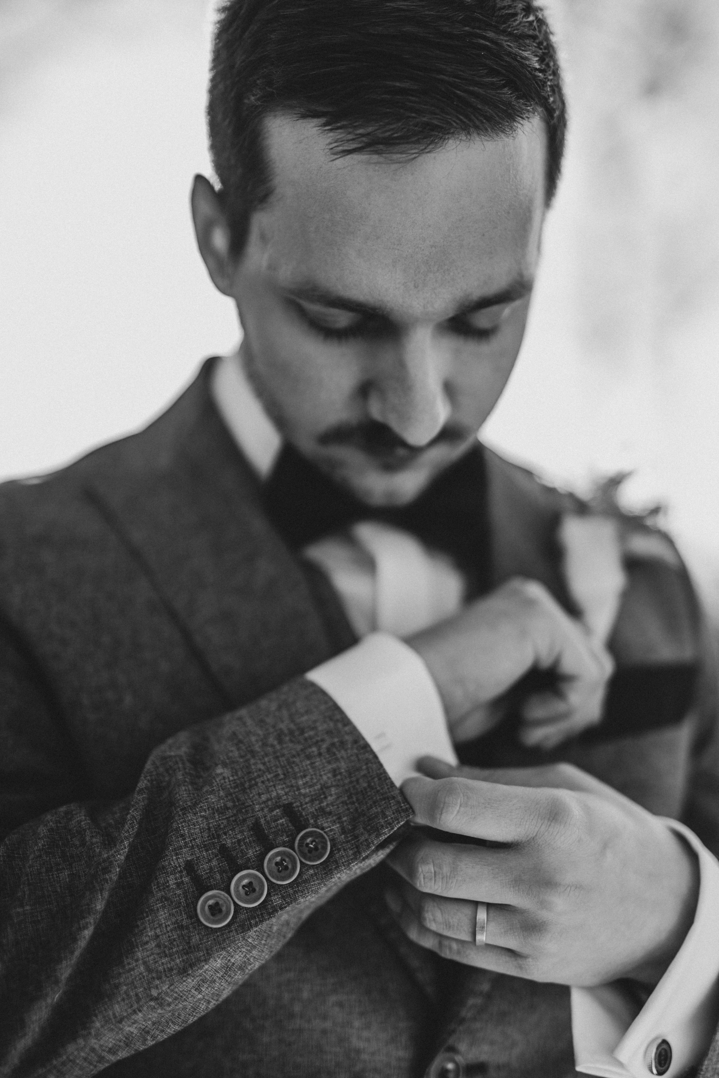 Black and white close-up of wedding rings on a tweed suit jacket.