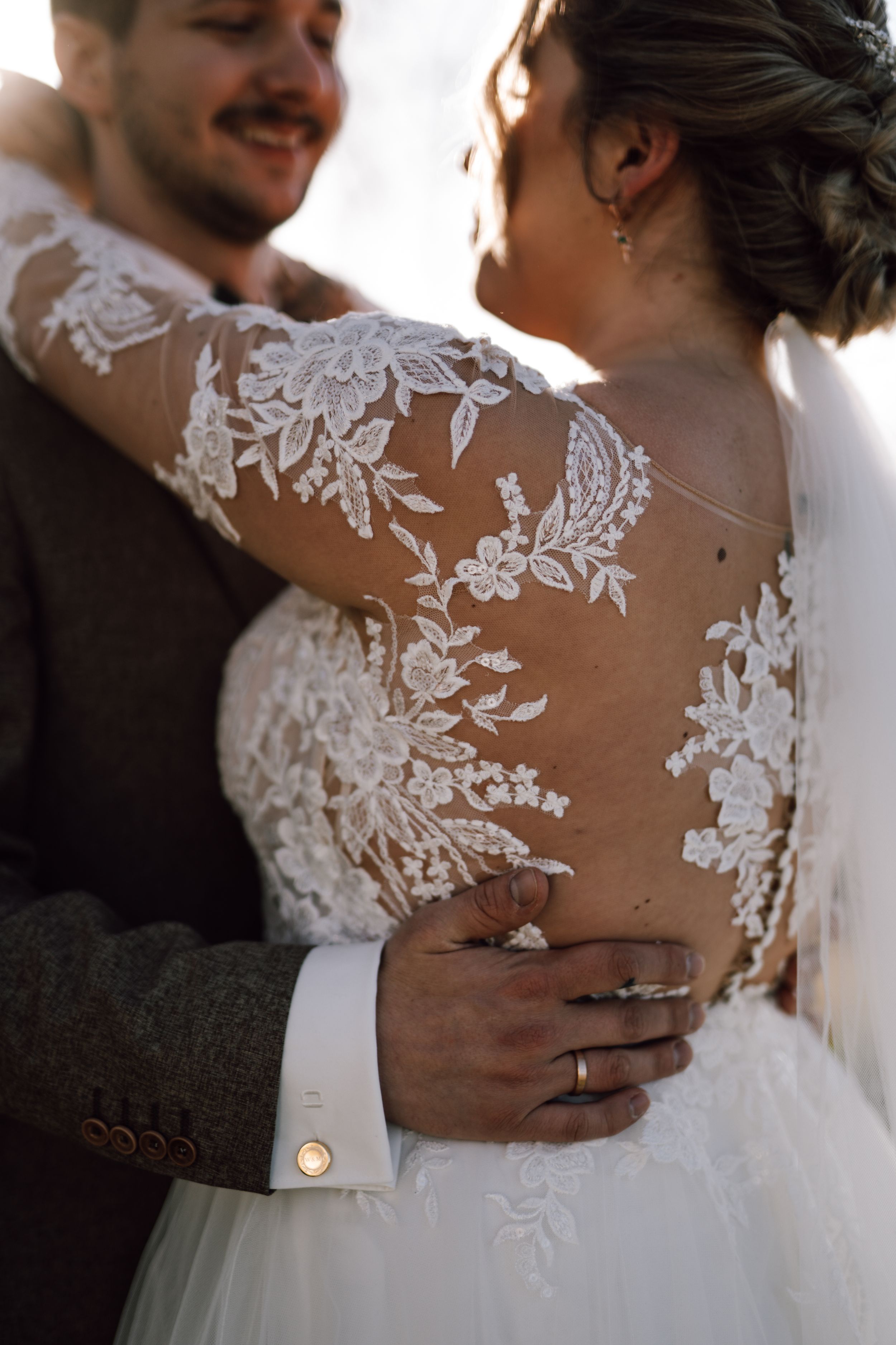 Delicate lace details on a wedding dress back as couple embraces.