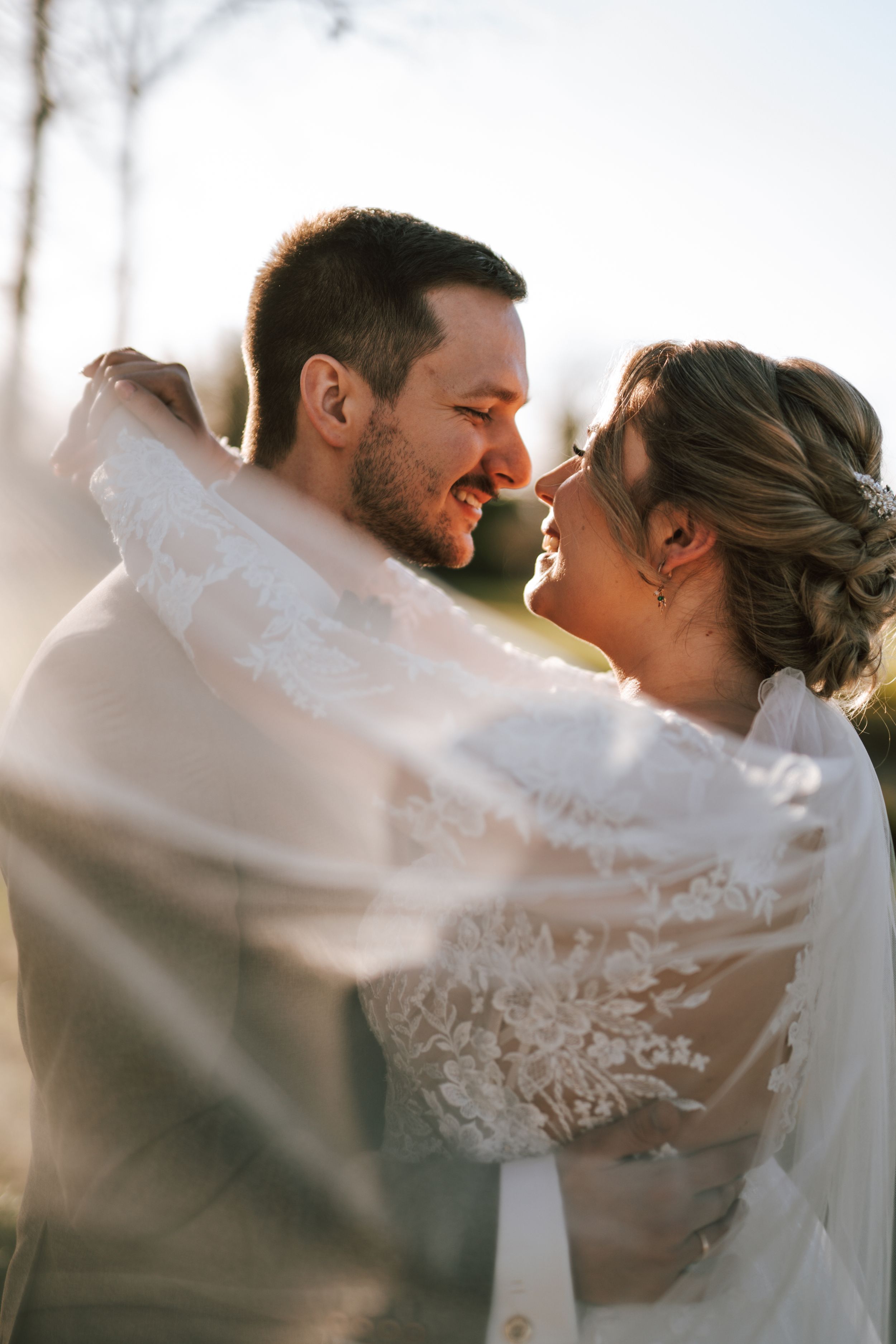 Romantic moment captured in soft sunlight with flowing white lace veil.